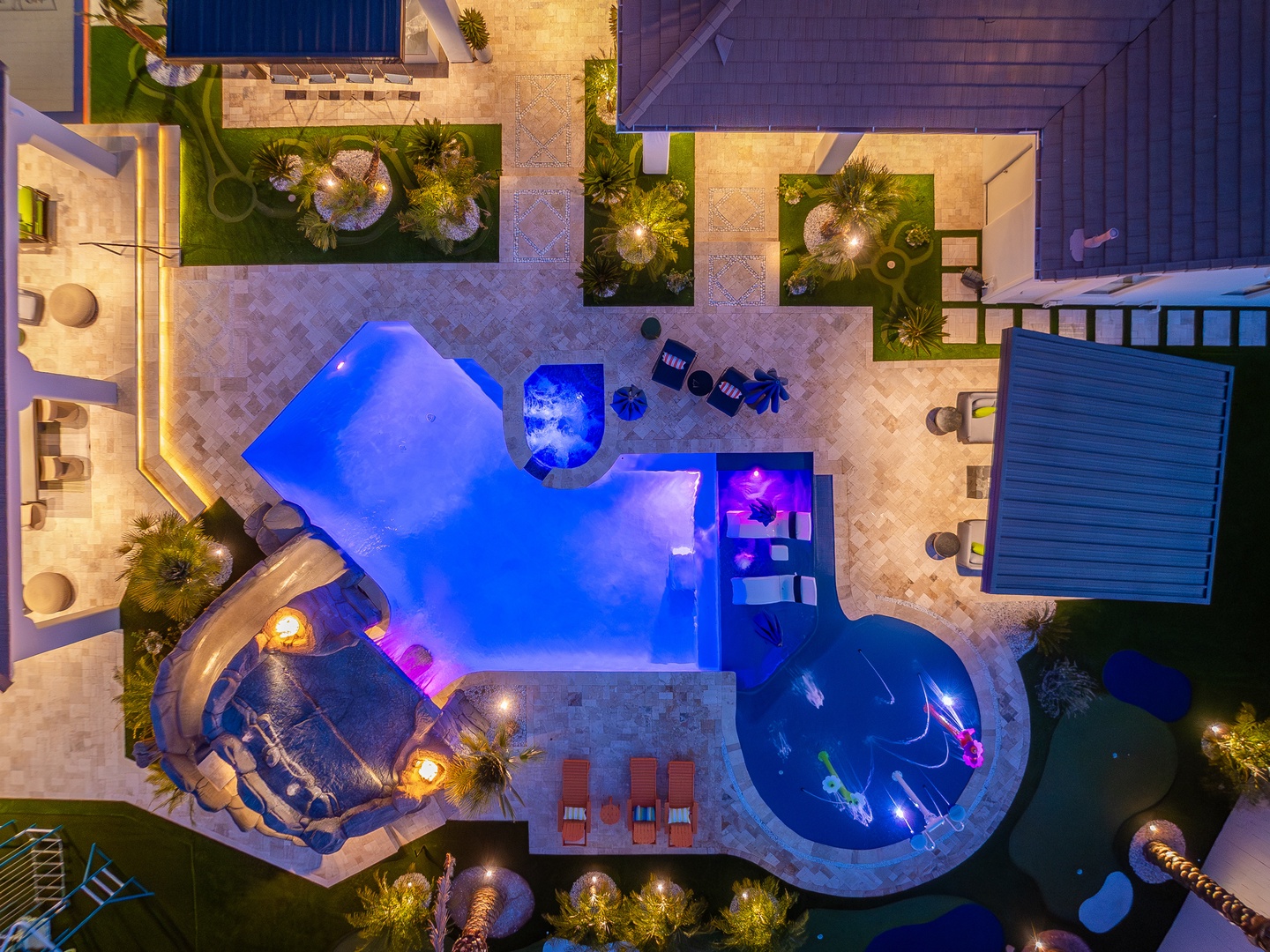 Aerial view of a resort-style property featuring illuminated swimming pools, tropical landscaping, and multiple lounging areas with evening lighting highlighting the architectural design and outdoor amenities.