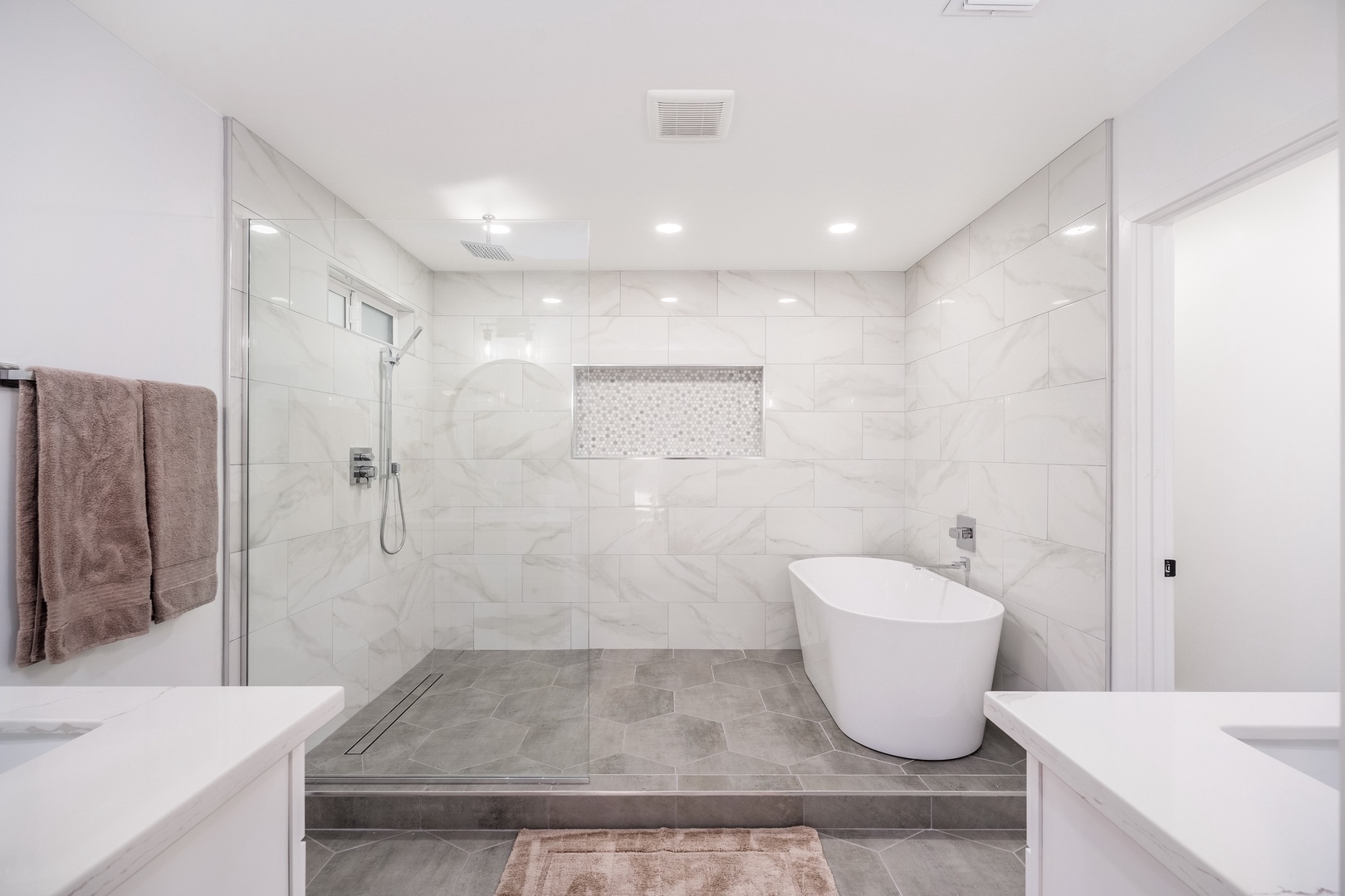 Immerse yourself in this pristine spa-like bathroom with elegant marble-look tiles, a sleek freestanding tub, and a spacious walk-in shower with rainfall head—your private retreat awaits.