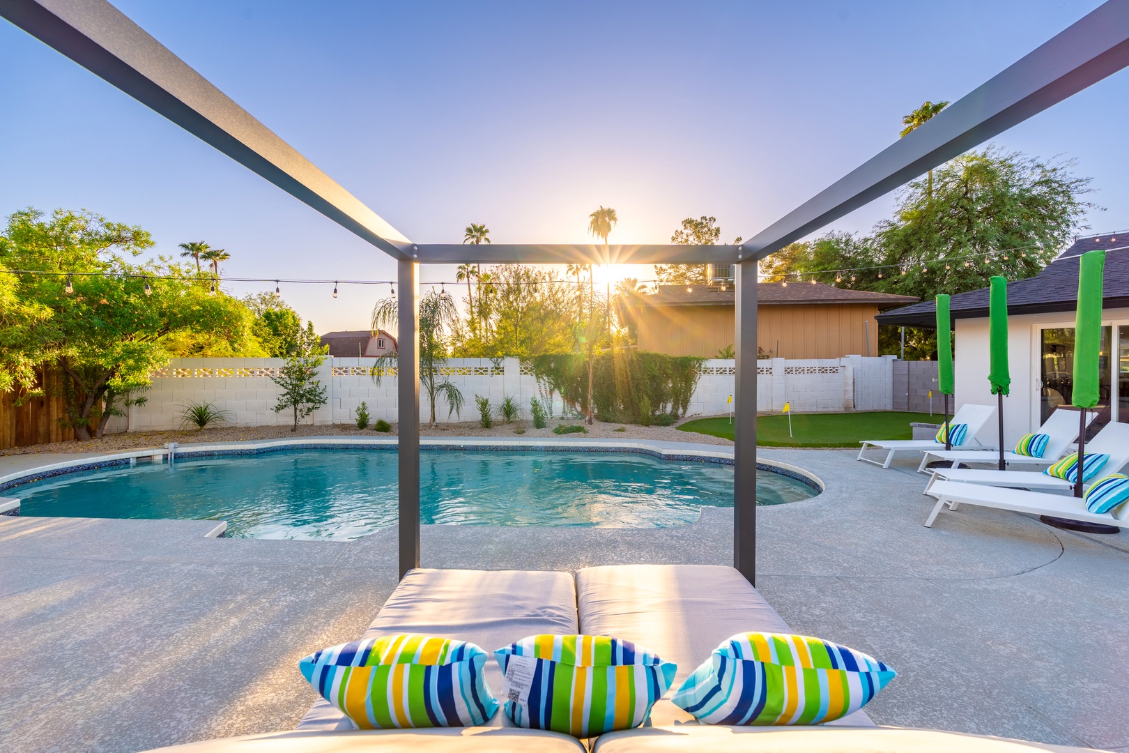 This sparkling pool at sunset offers your private oasis, framed by swaying palms and modern shade structures, with vibrant loungers ready for sun-soaked afternoons.