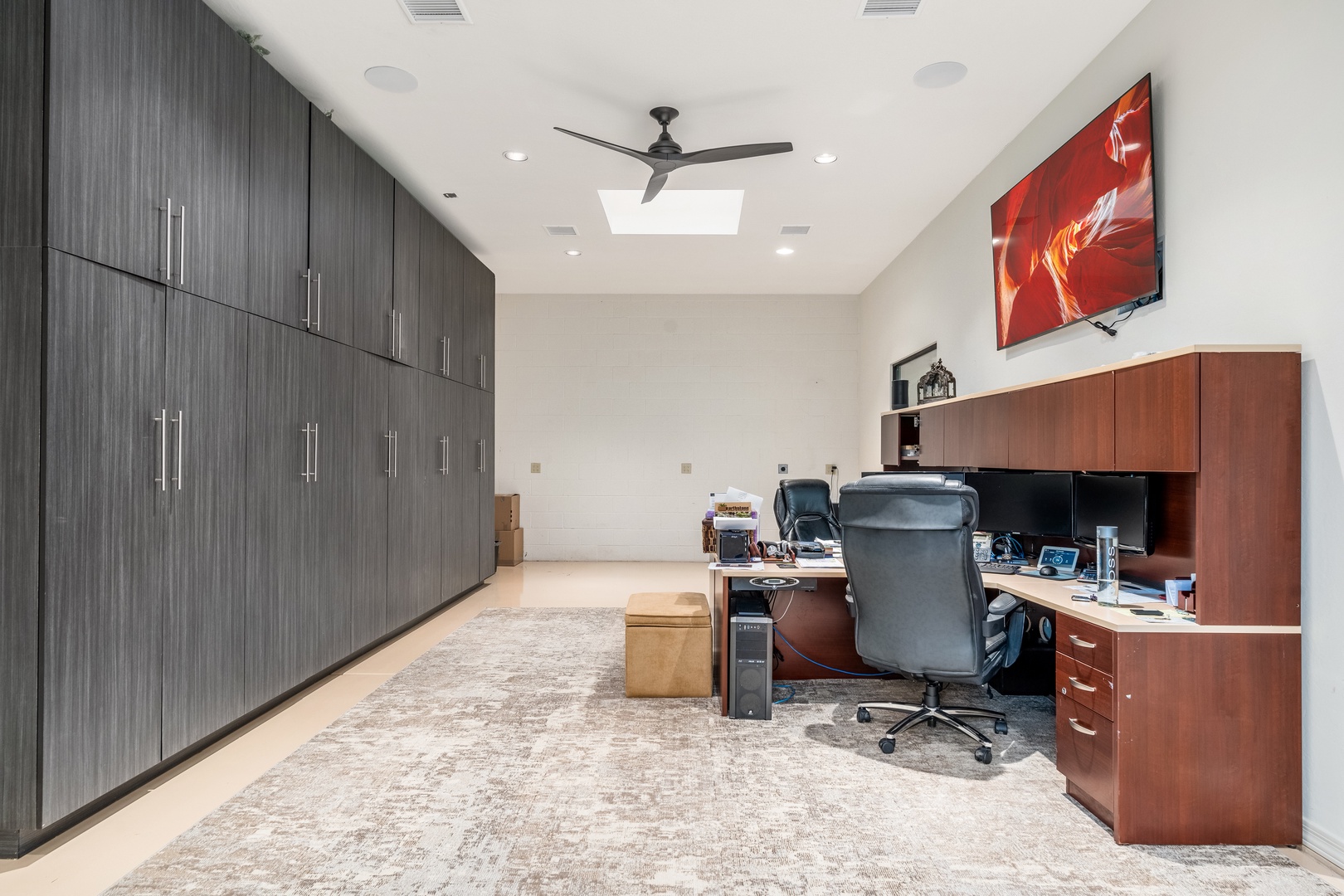 A sleek, modern office space with generous storage awaits your workday, featuring a built-in desk, ceiling fan, and skylight overhead to keep you comfortable and inspired.