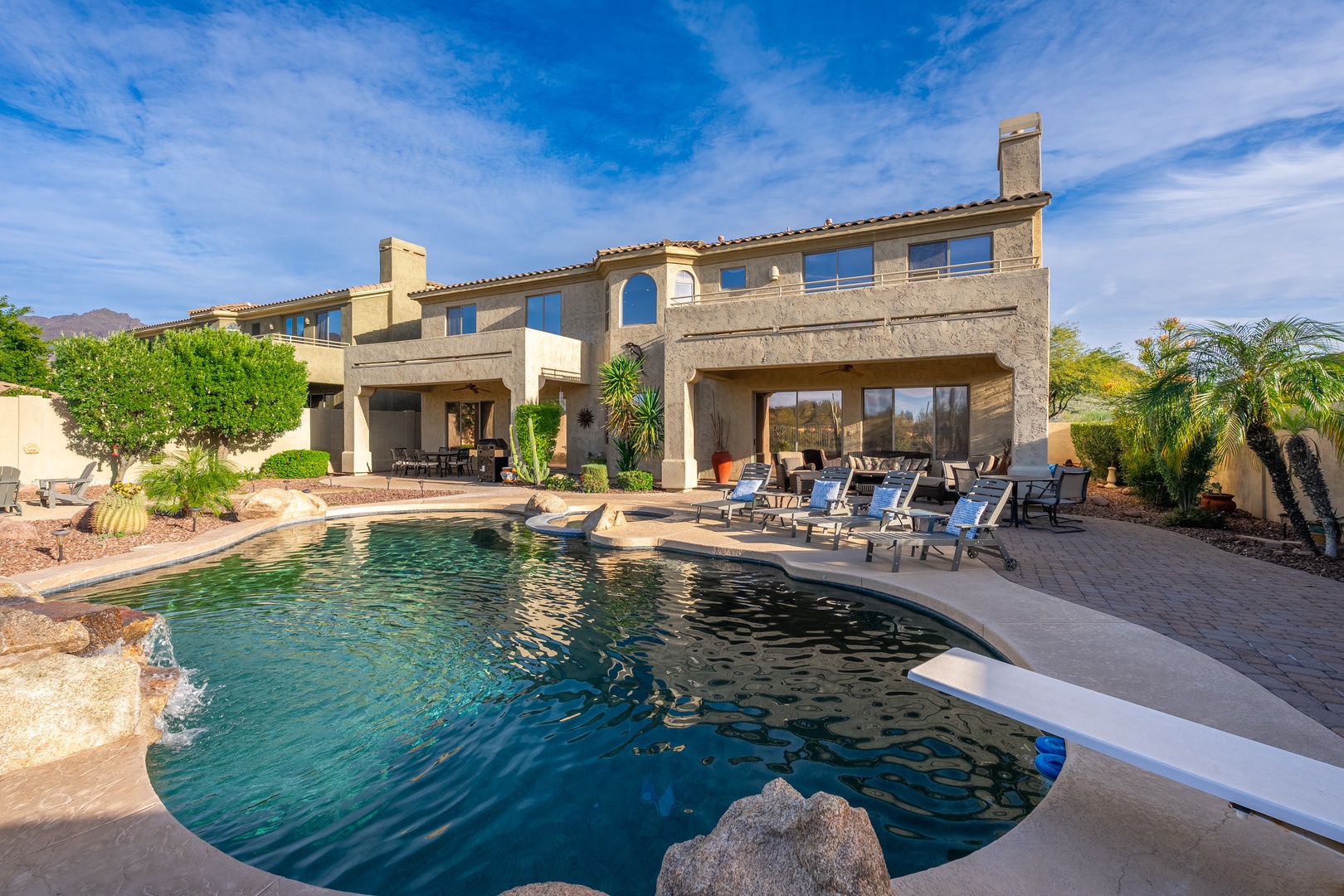 Expansive desert villa showcasing elegant southwestern architecture, a sparkling freeform pool with rock features, and mountain views—ideal arrival setting for an elevated escape.