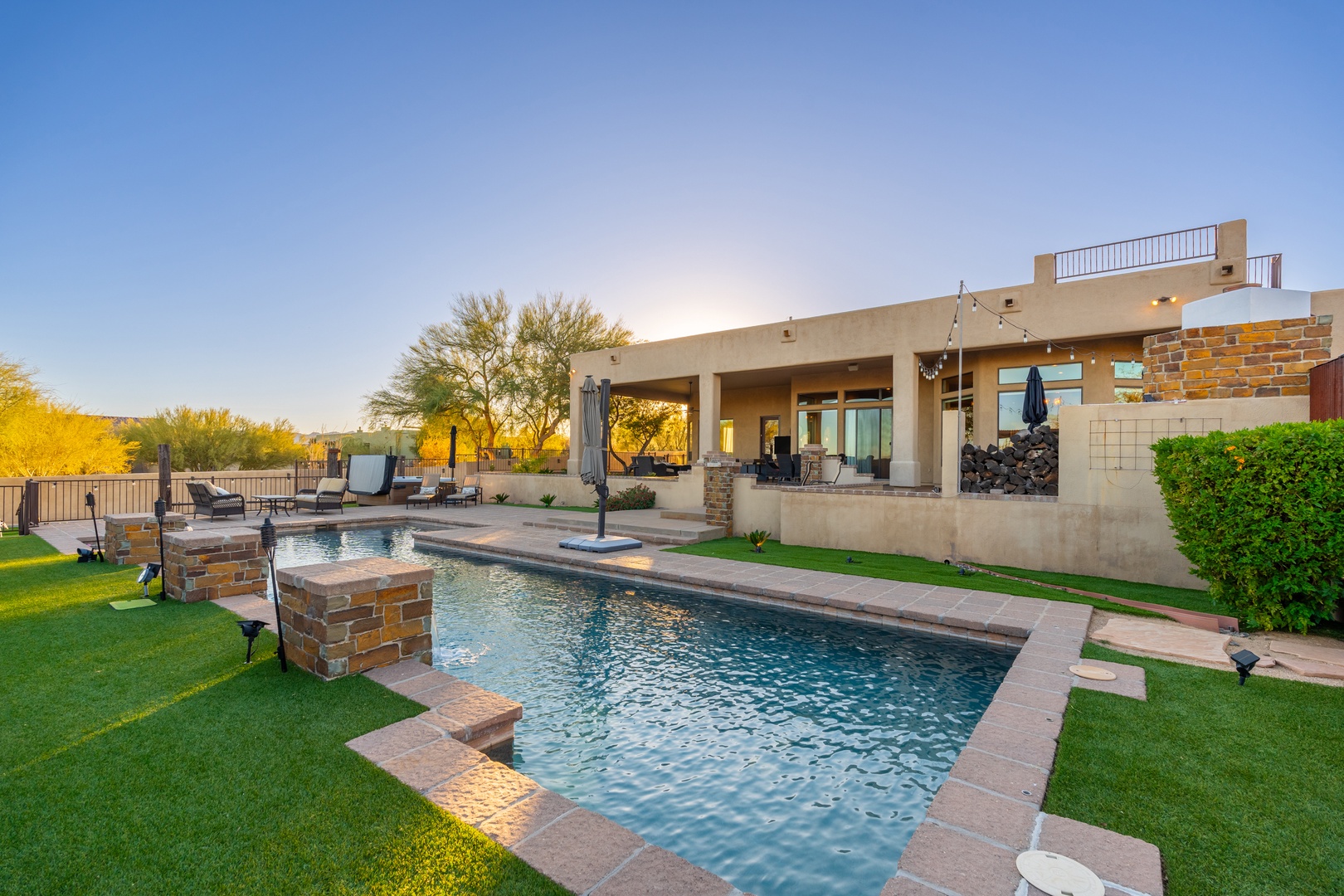 Modern desert retreat showcasing a sparkling pool, spacious patio, and rooftop deck. The property sits amid natural desert landscape with mountain views at golden hour.