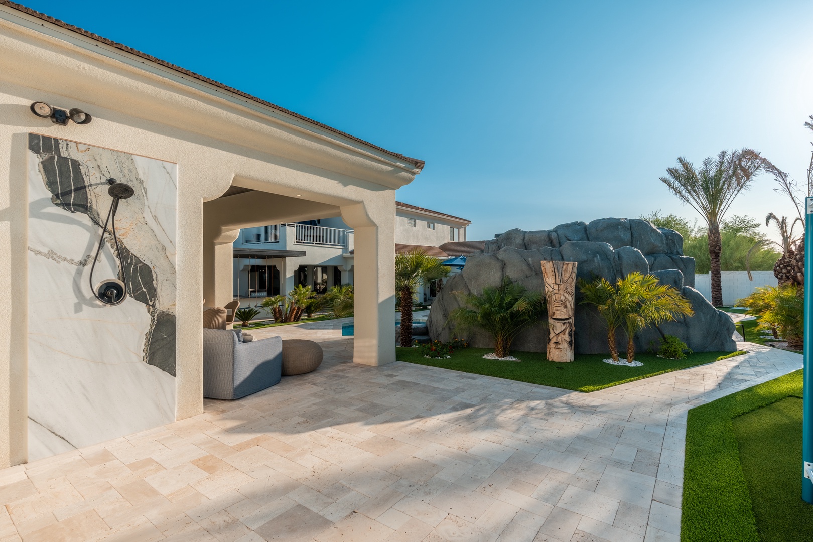 A distinctive vacation property featuring a tropical desert landscape with palm trees, sculptural rock formations, and a paved courtyard leading to multiple buildings and a pool area.