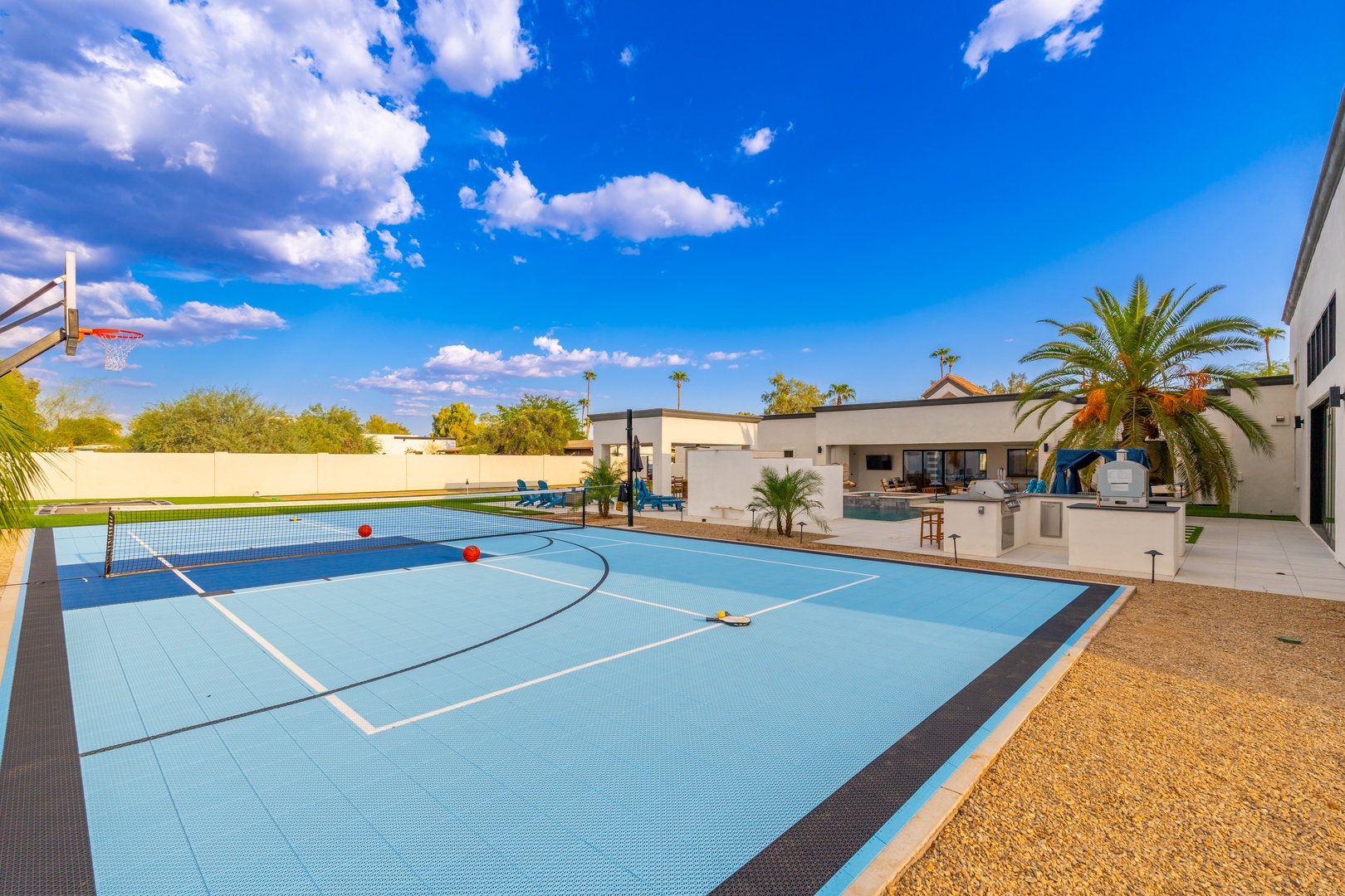 Modern desert estate offering a full-size sport court and sparkling pool amid lush palm trees and Arizona sunshine, perfect for active relaxation.