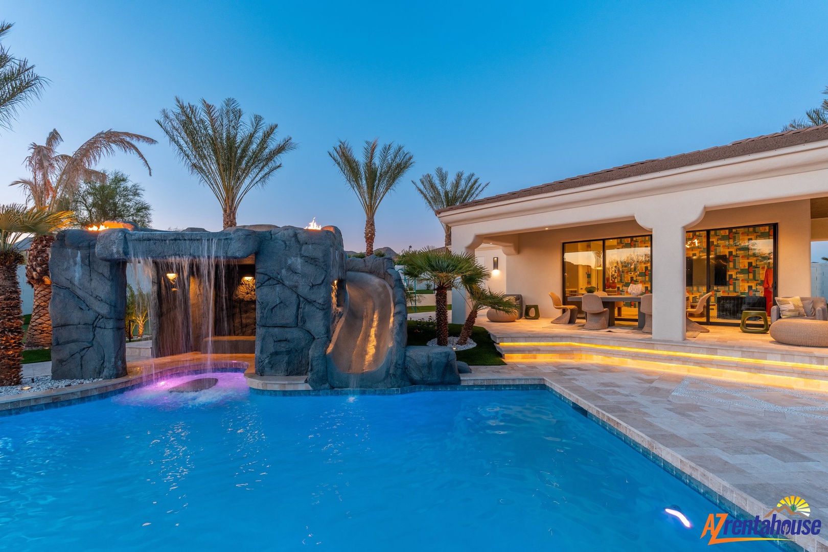 Luxury pool with waterfall grotto and slide creates your private resort oasis beneath swaying palms and desert sky.