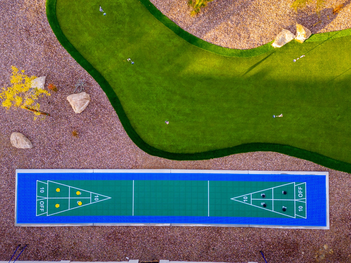 Aerial view of the property's recreational area featuring a putting green and outdoor shuffleboard court, surrounded by scenic desert landscaping with natural rock formations and native vegetation.