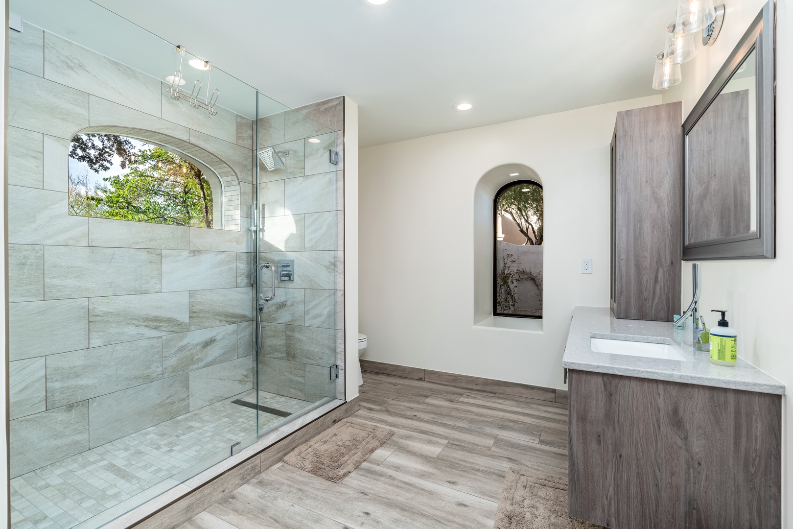 Step into your tranquil retreat with a spa-like walk-in shower wrapped in elegant stone tile and a stylish vanity beneath soft pendant lighting—your personal sanctuary awaits.