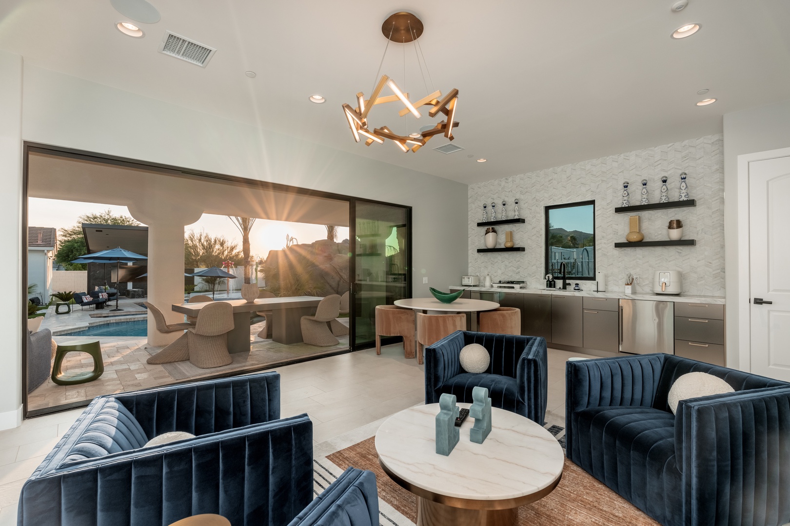 Your retreat opens to a serene desert sunset through floor-to-ceiling glass, where stylish lounge seating invites you to unwind while the pool sparkles just beyond reach.