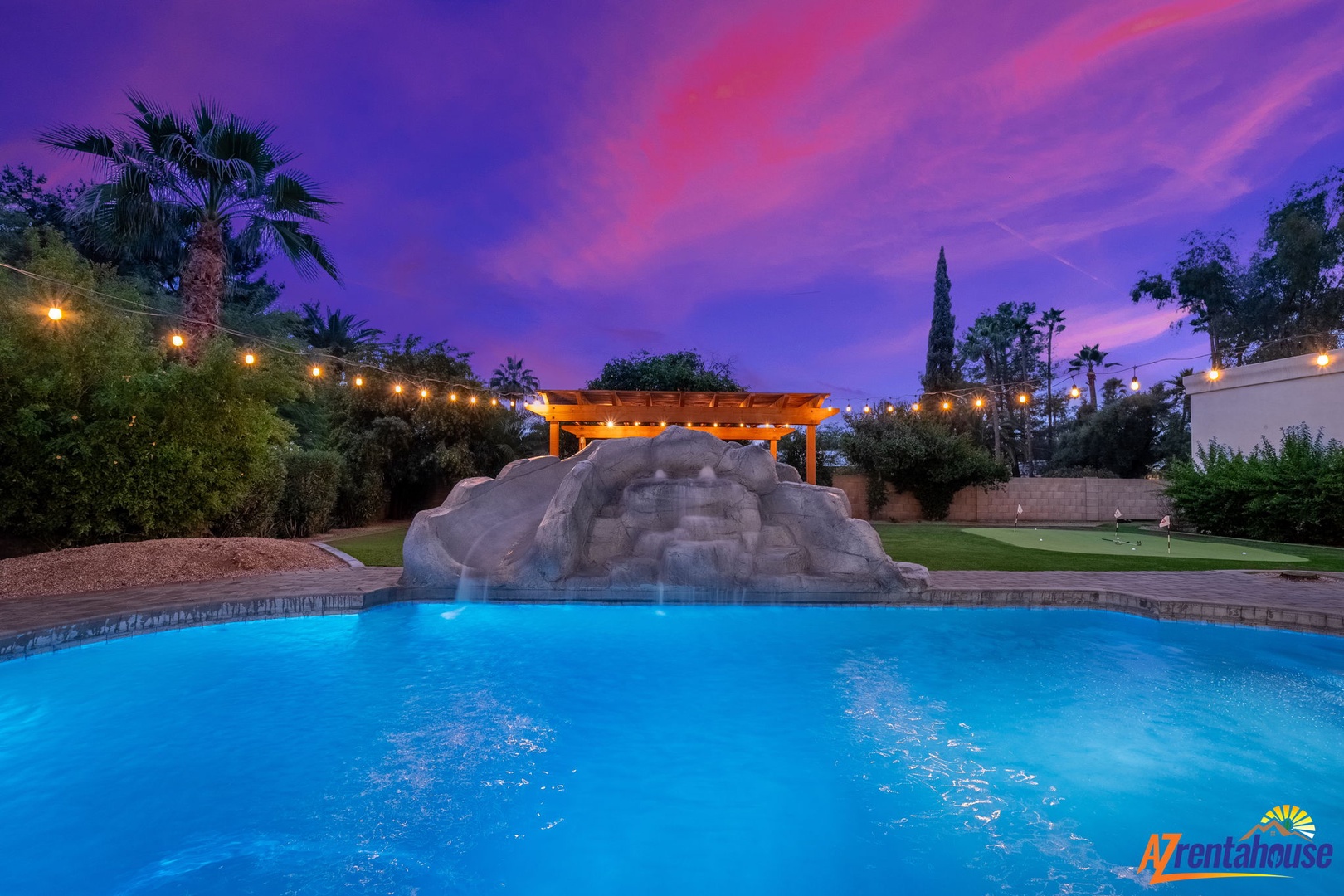 Spectacular twilight colors paint the sky above this resort-style pool with rock waterfall feature and tropical landscaping.