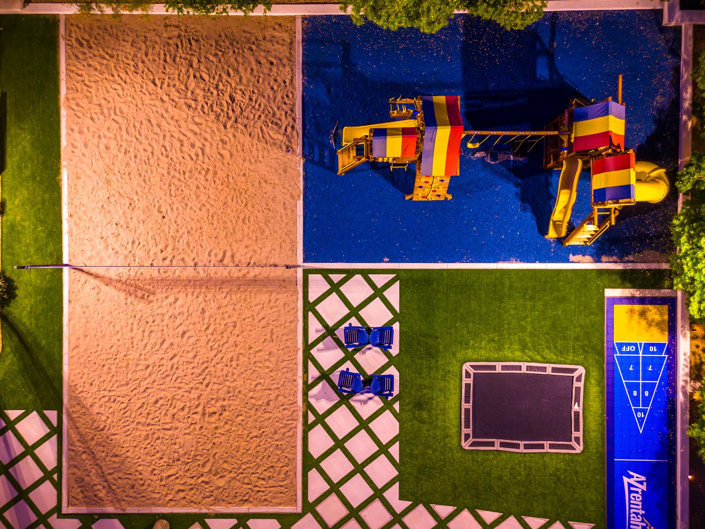 Aerial view of the property's recreational area featuring a vibrant swimming pool, colorful inflatable water park, sandy play zone, outdoor games area, and sunbathing deck surrounded by lush greenery.