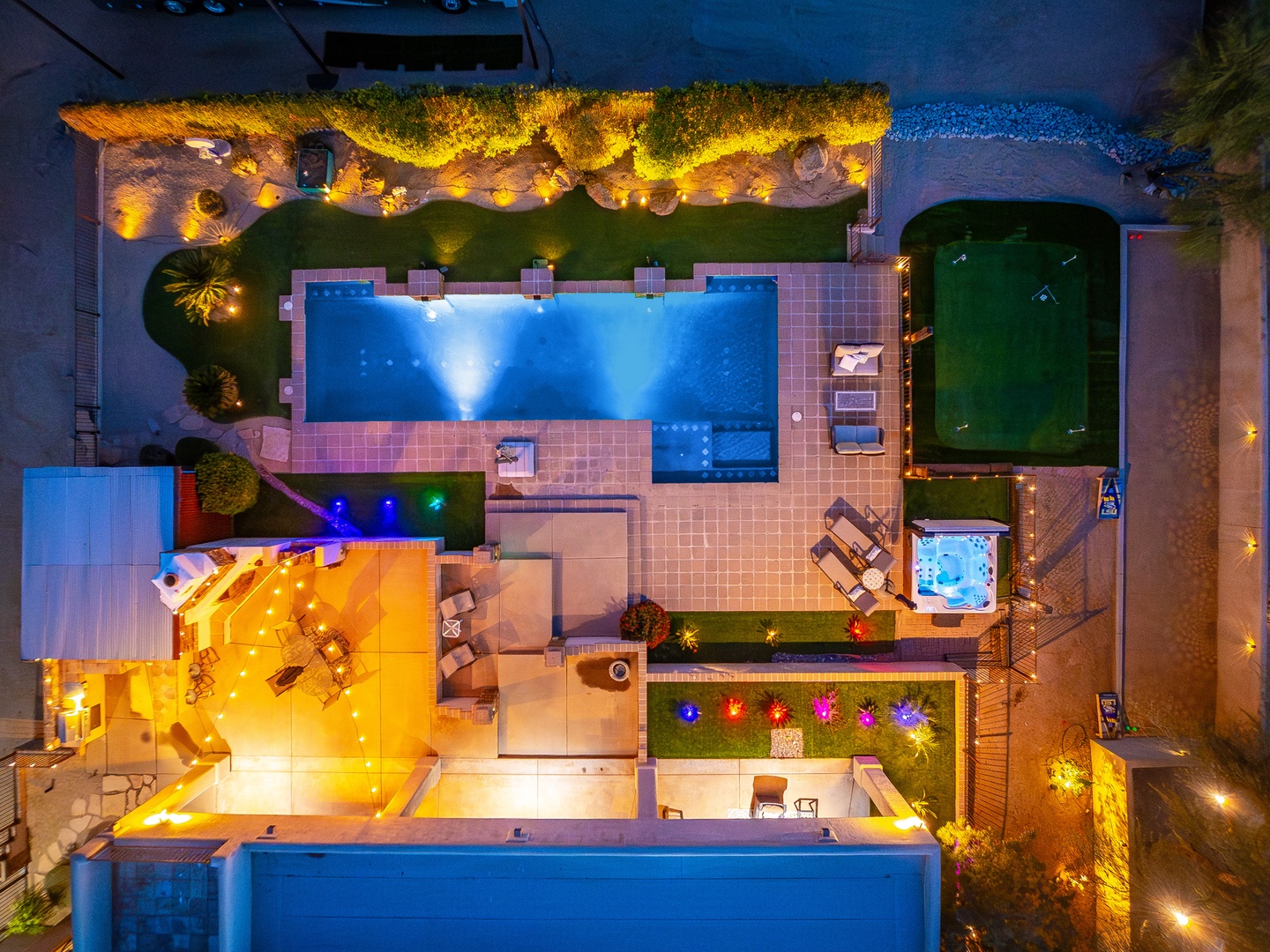 Stunning aerial view of the villa reveals an outdoor paradise: sparkling pool, intimate hot tub, lush garden spaces, and atmospheric evening lighting create an exceptional vacation retreat.