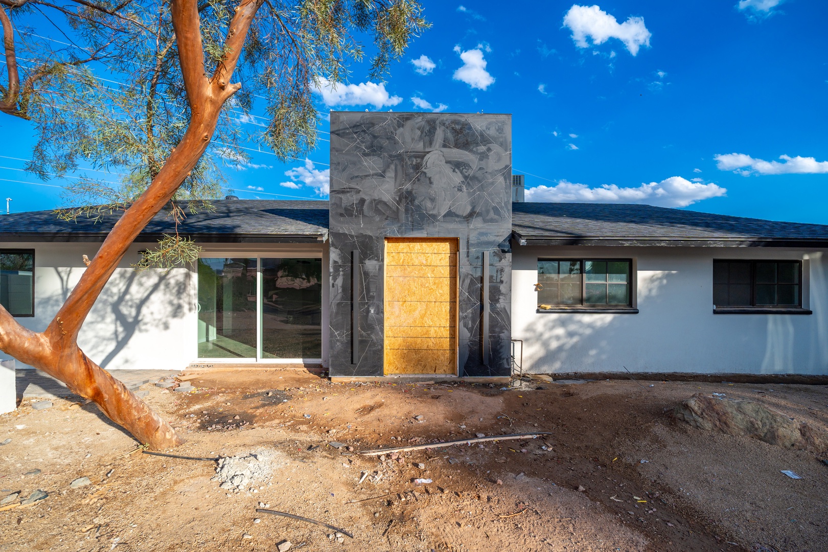 This modern desert retreat features striking dark stone accents and a glowing entrance beneath bright blue skies and native trees.