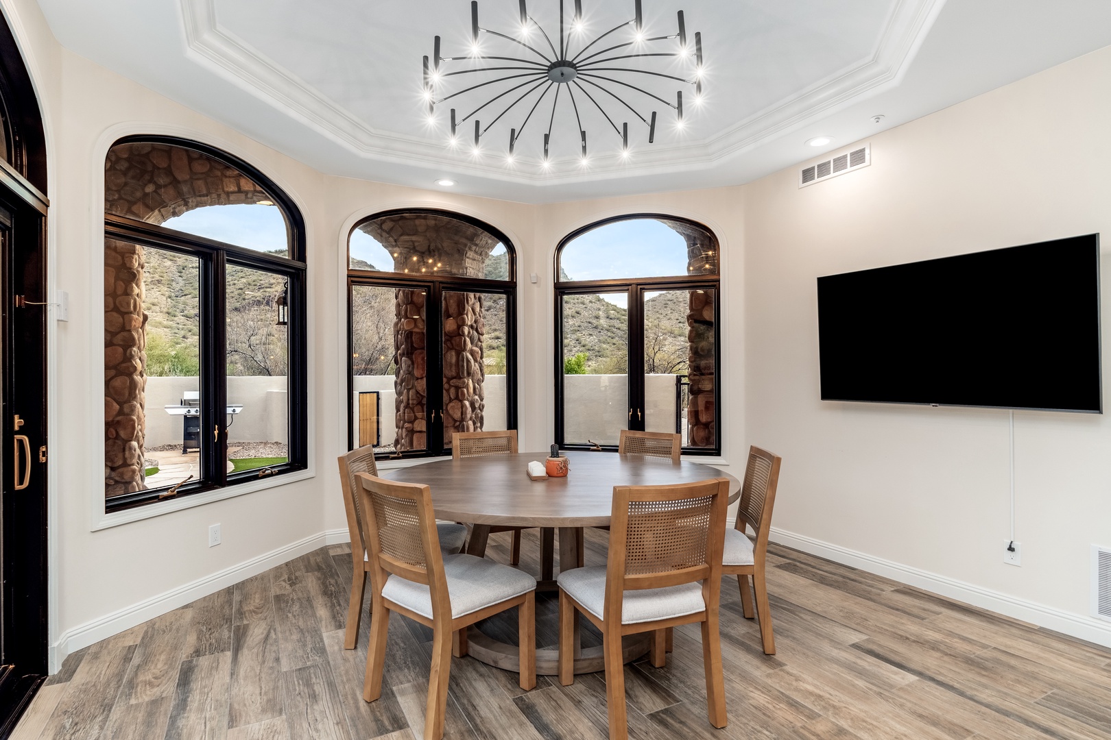 Gather around this elegant dining table beneath a stunning chandelier. Arched windows frame desert mountain views, blending indoor comfort with natural beauty—your perfect setting for memorable meals.