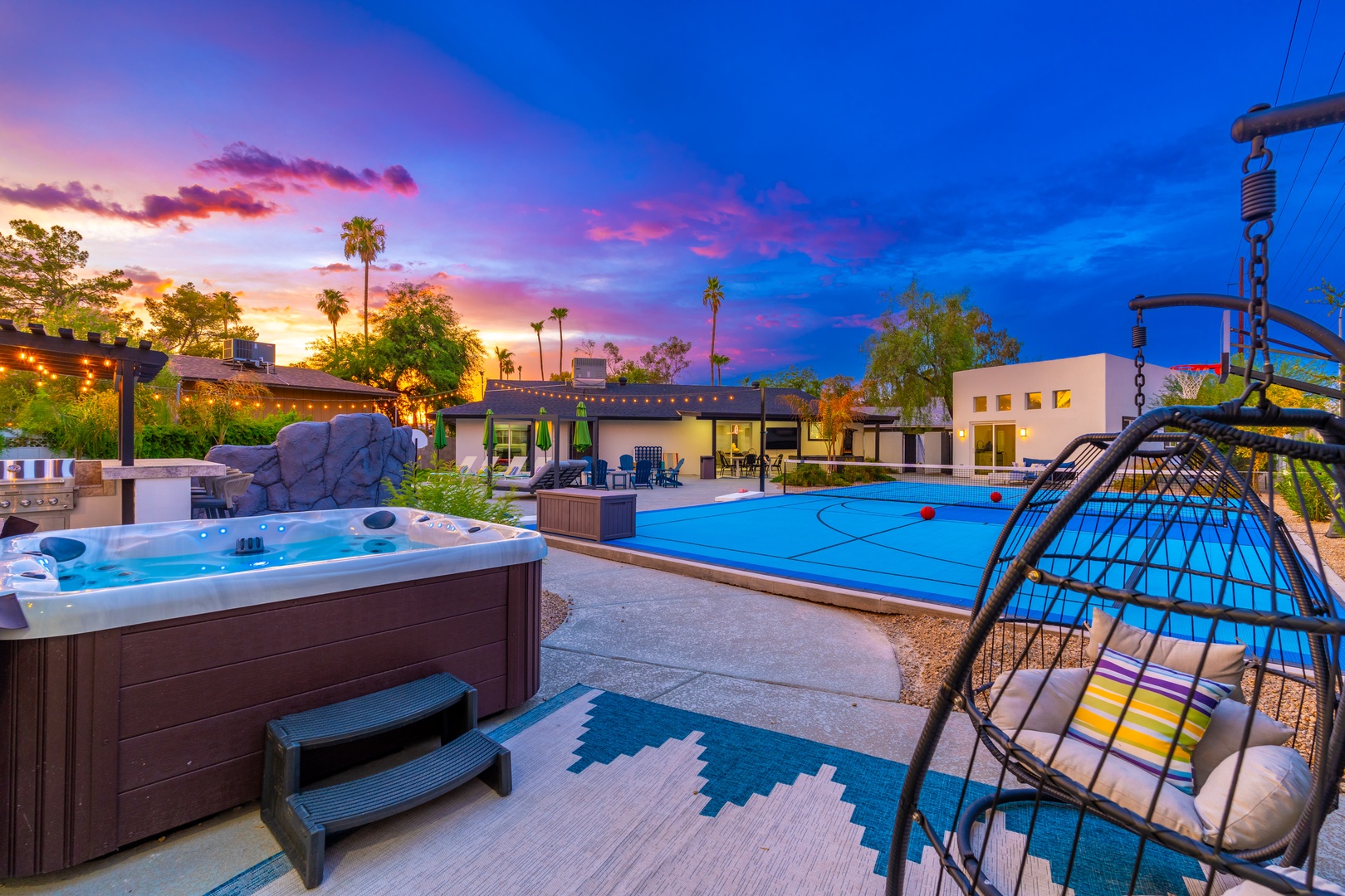 A dramatic desert sunset paints the sky while the property and surrounding palm trees glow in the evening light, with the pool area visible in the distance.