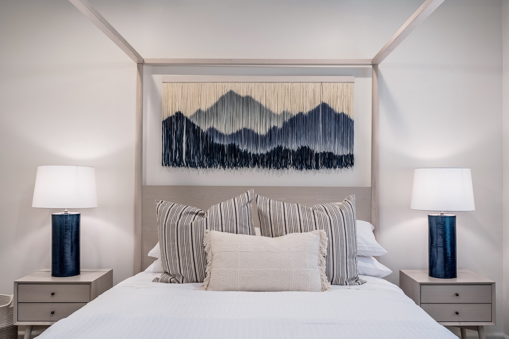 Sink into crisp white linens framed by a stunning mountain tapestry—your restful retreat awaits with calming blues, soft lighting, and thoughtful decor that makes relaxation effortless.