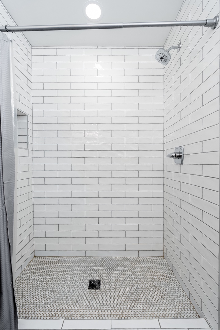 Step into a pristine shower with crisp white subway tiles and a rainfall showerhead, designed for your refreshing daily ritual.