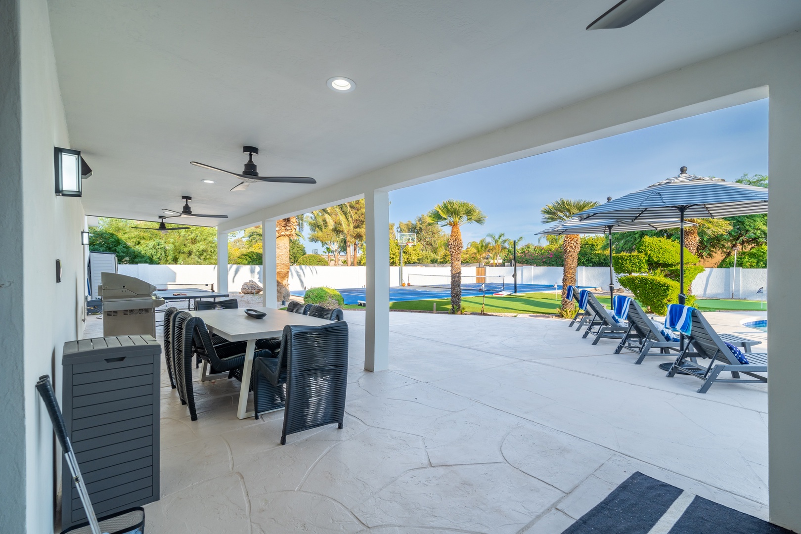 Relax and dine under the covered patio with ceiling fans, enjoying seamless access to your private pool, sunny lawn, and lush palm-lined backyard retreat.