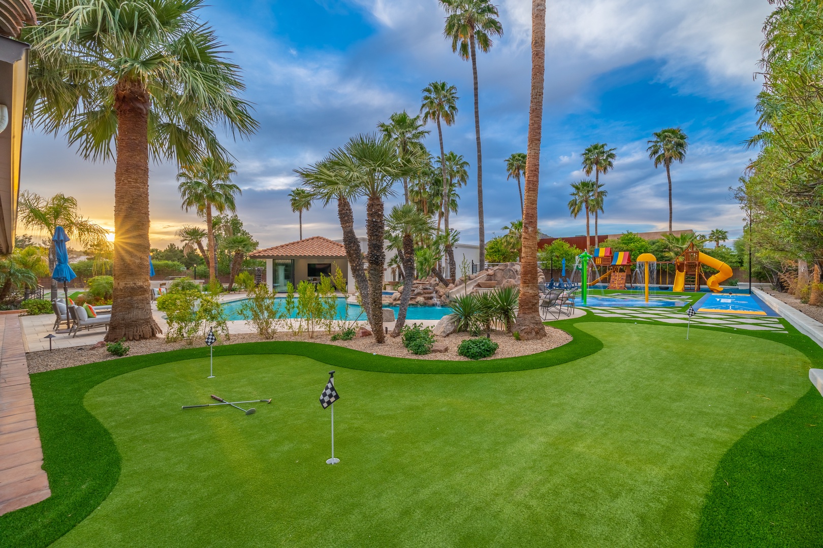 Luxury estate featuring private putting green, sparkling pool, and colorful water play area surrounded by towering palms—a desert oasis perfect for memorable family getaways.
