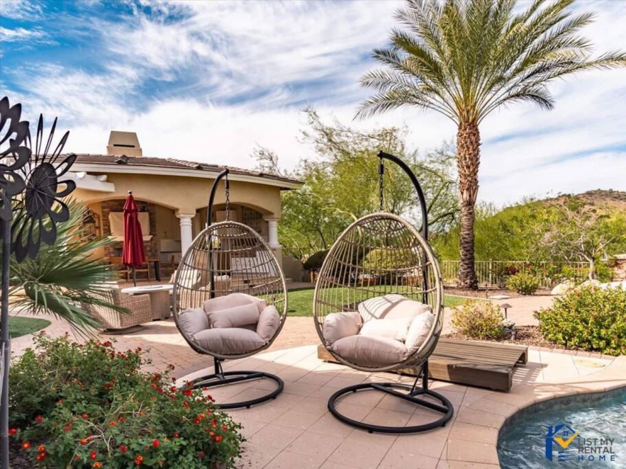 Desert retreat with hanging egg chairs and palm tree, surrounded by mountain views and landscaped grounds.