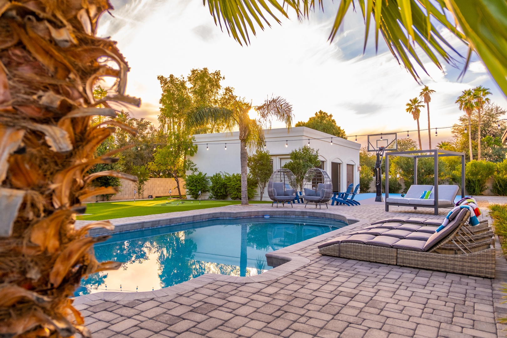 A serene desert oasis at golden hour, showcasing modern architecture surrounded by mature palms and lush landscaping in a peaceful residential setting.
