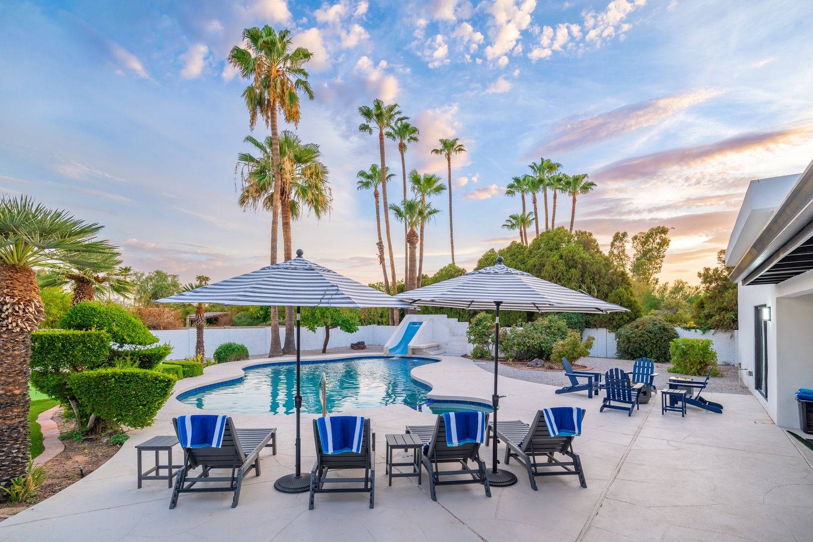 Towering palms frame the sparkling pool where blue loungers and umbrellas invite you to unwind. Slide into refreshing water or lounge poolside beneath desert skies, surrounded by lush landscaping and peaceful desert beauty.