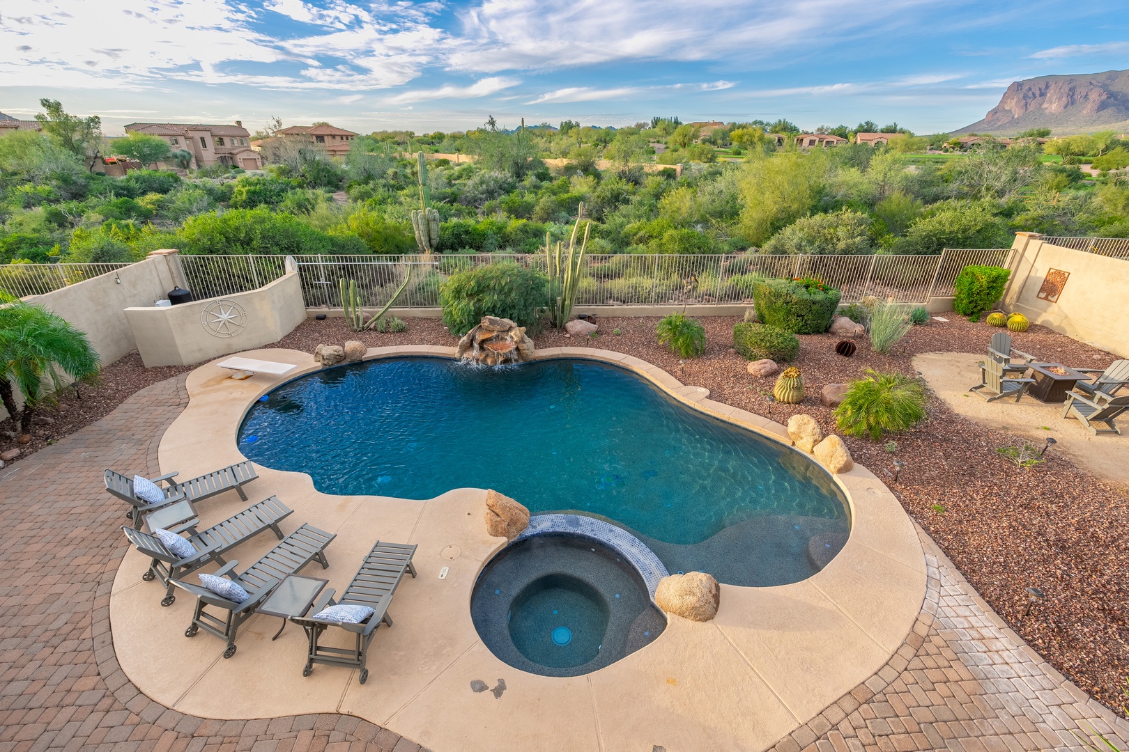 An aerial view of the property showcasing the private pool and hot tub surrounded by desert landscaping, with mountain vistas and lush green vegetation in the background.