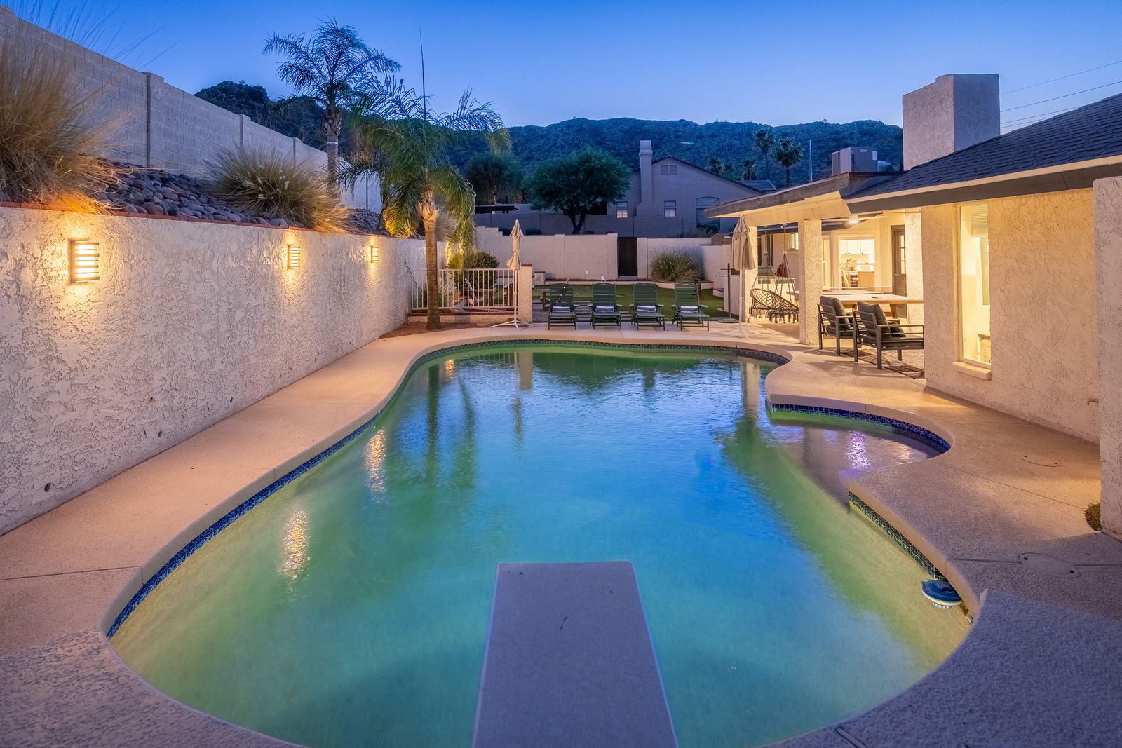 Twilight glow surrounds your private pool oasis, complete with loungers, mountain views, and warm ambient lighting along the stucco walls—perfect for evening swims under the stars.