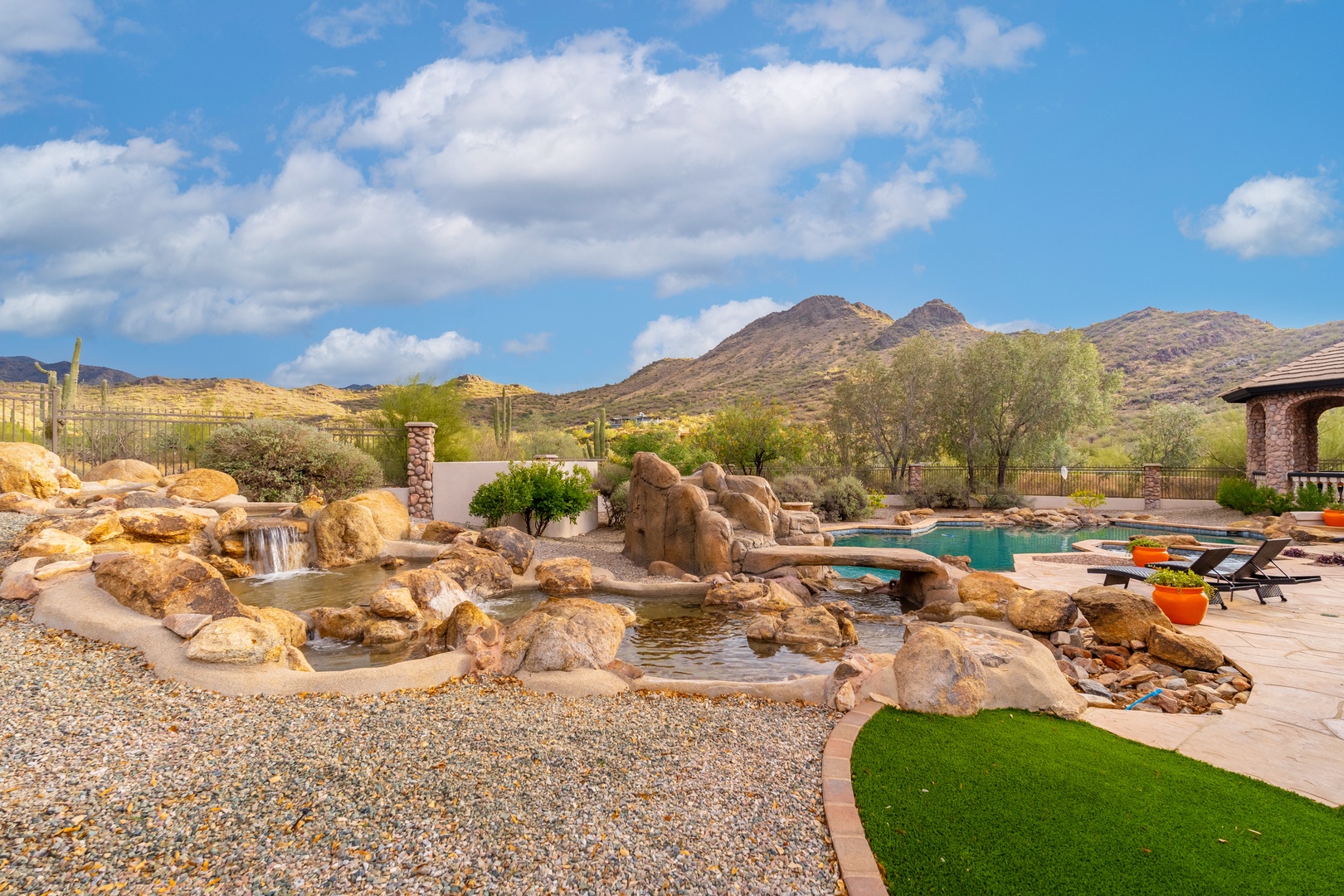 A stunning desert resort backdrop featuring dramatic mountain peaks, native landscaping, and tiered water features that frame the pool area—an authentic Arizona escape surrounded by natural beauty.
