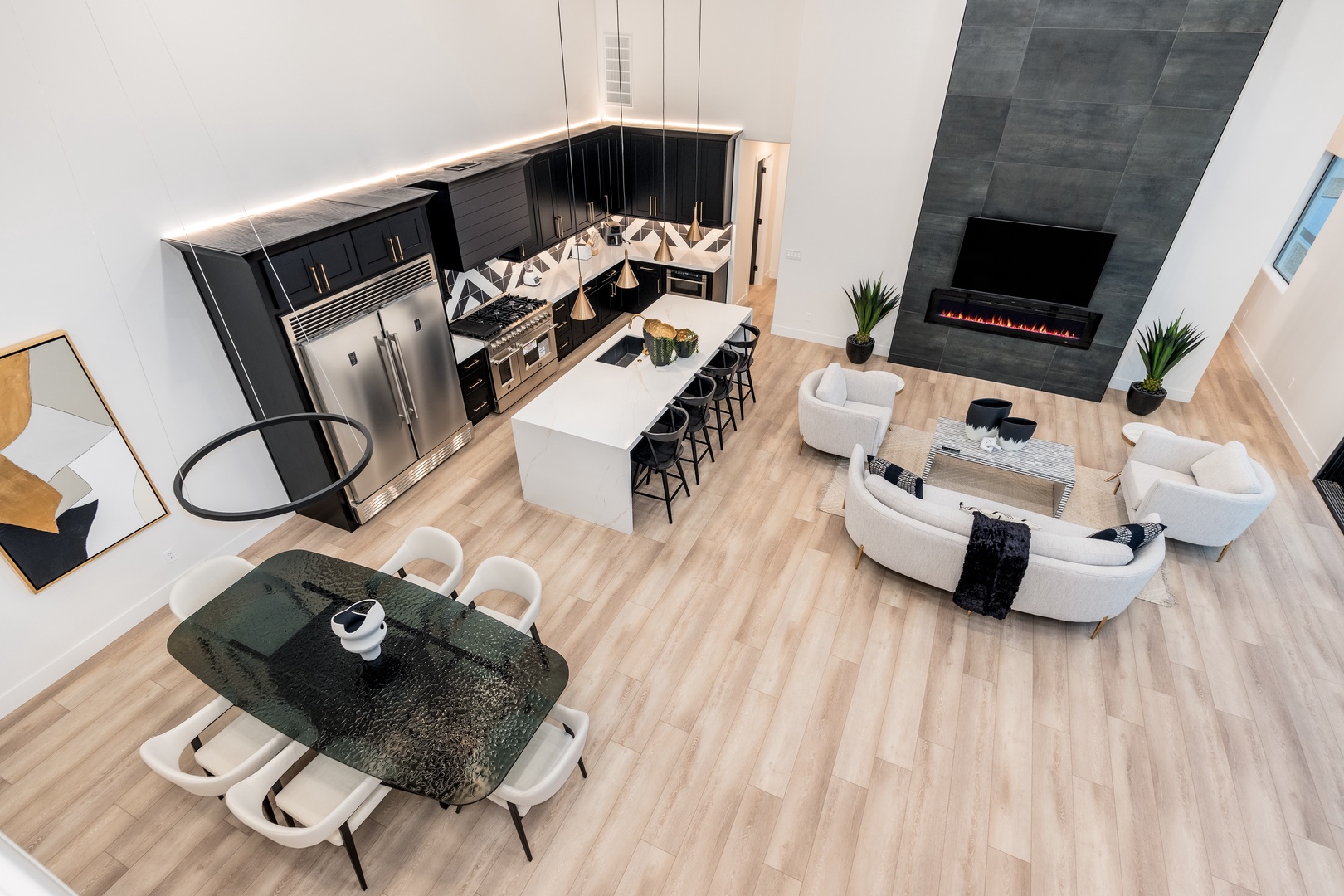 Soaring ceilings and sleek design define this open-concept space where your chef's kitchen, modern dining area, and cozy living room flow seamlessly beneath dramatic pendant lighting and a stunning fireplace feature.