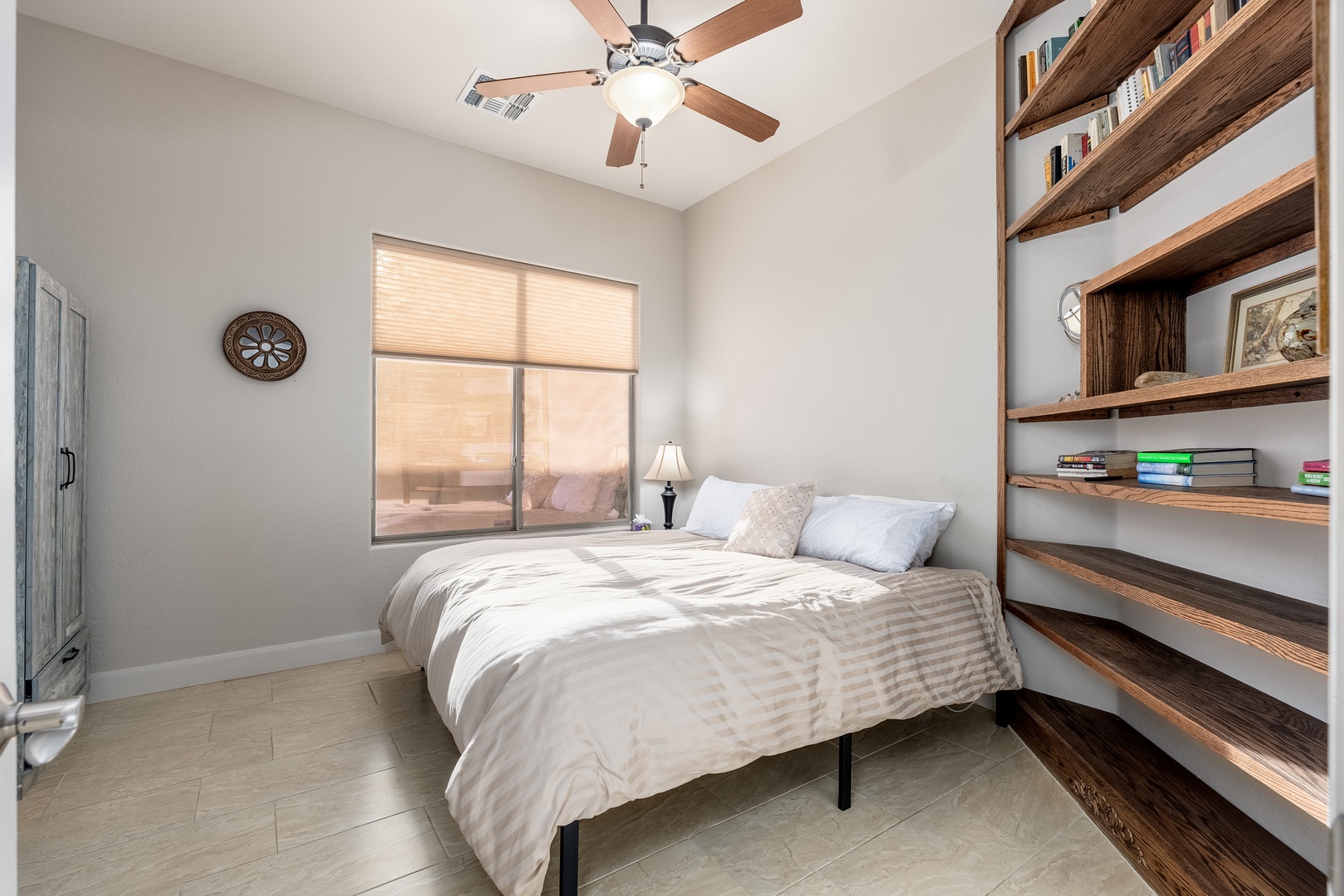 Drift off beneath the gently spinning ceiling fan in this tranquil bedroom, where warm wood shelving and soft natural light create a peaceful retreat for your stay.