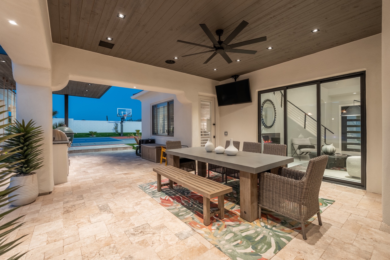 This covered patio is your perfect spot for outdoor meals and relaxation. Dine under the warm glow of recessed lighting, cooled by a ceiling fan, with views of the pool and basketball court.