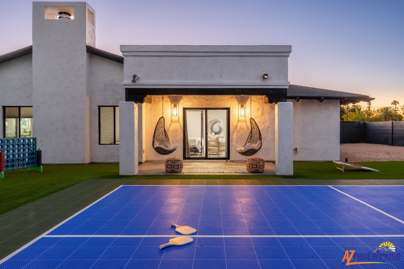 Modern vacation home featuring a covered patio with hanging chairs, swimming pool, and contemporary design elements at sunset.