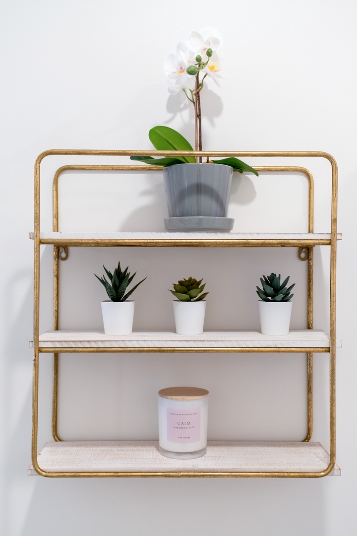 Stylish gold-framed shelf holds calming greenery—delicate orchids and succulents accent this peaceful corner, complemented by a soothing scented candle for your moments of tranquility.