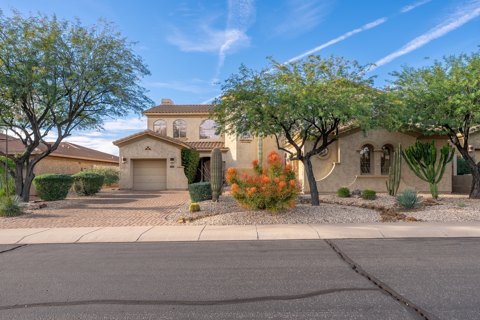 Southwestern-style property featuring desert landscaping with mature trees, cacti, and native plants. The stucco exterior and tile roof complement the surrounding residential neighborhood.