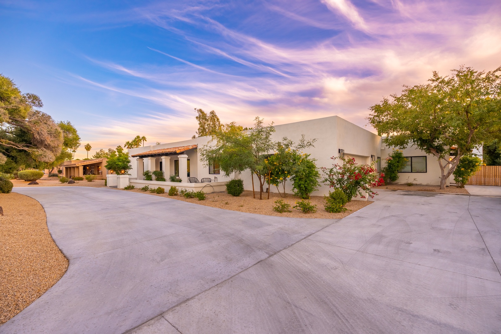 Modern desert retreat featuring spacious paved parking and inviting southwestern architecture set against a stunning desert sky at dusk.