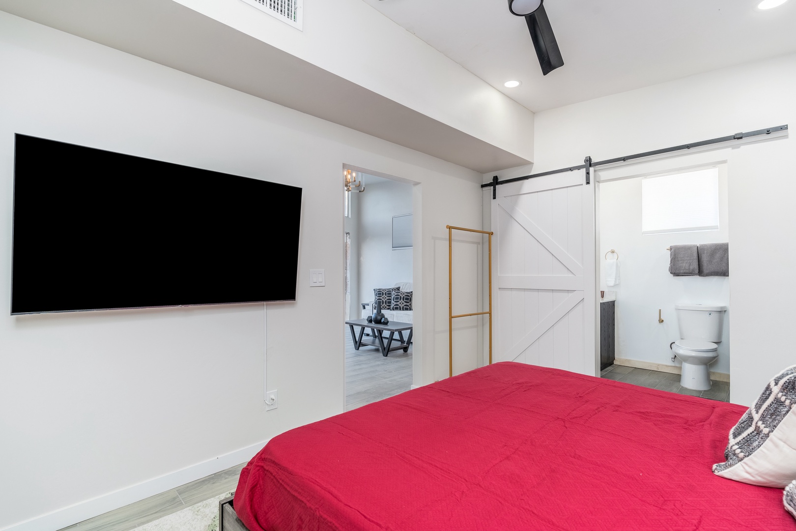 Unwind in your airy, modern bedroom featuring a plush bed, wall-mounted TV for cozy evenings, and a charming barn door opening to your private en-suite bathroom.