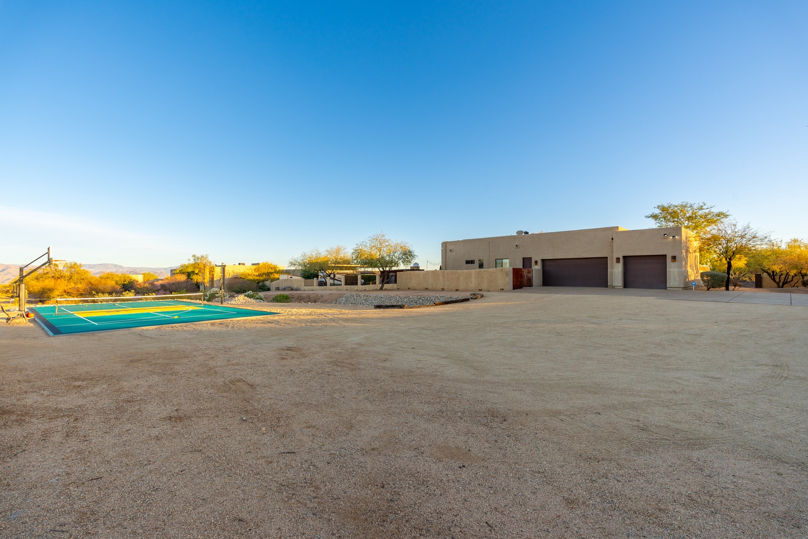 Desert property featuring sports court and spacious parking area, framed by natural landscape and mountain views under clear blue skies.