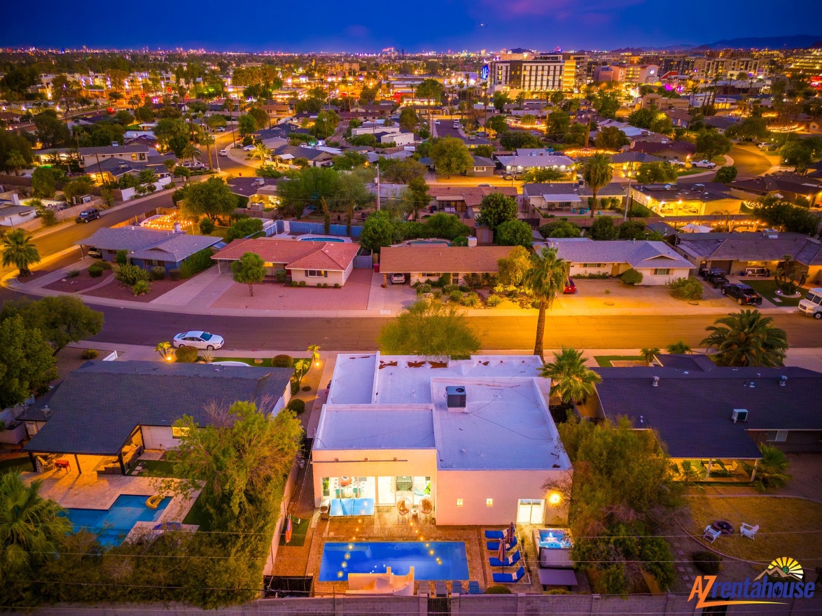 Aerial view of the property nestled in a vibrant residential neighborhood, illuminated against the evening skyline with city lights stretching to the horizon.