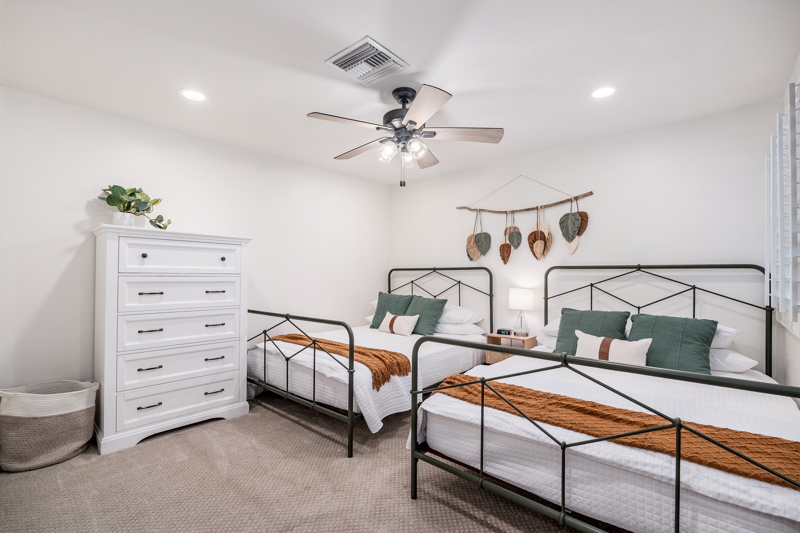 Your peaceful guest bedroom features two cozy beds with crisp linens, warm rust accents, and charming rustic wall decor. The ceiling fan keeps things comfortable year-round.