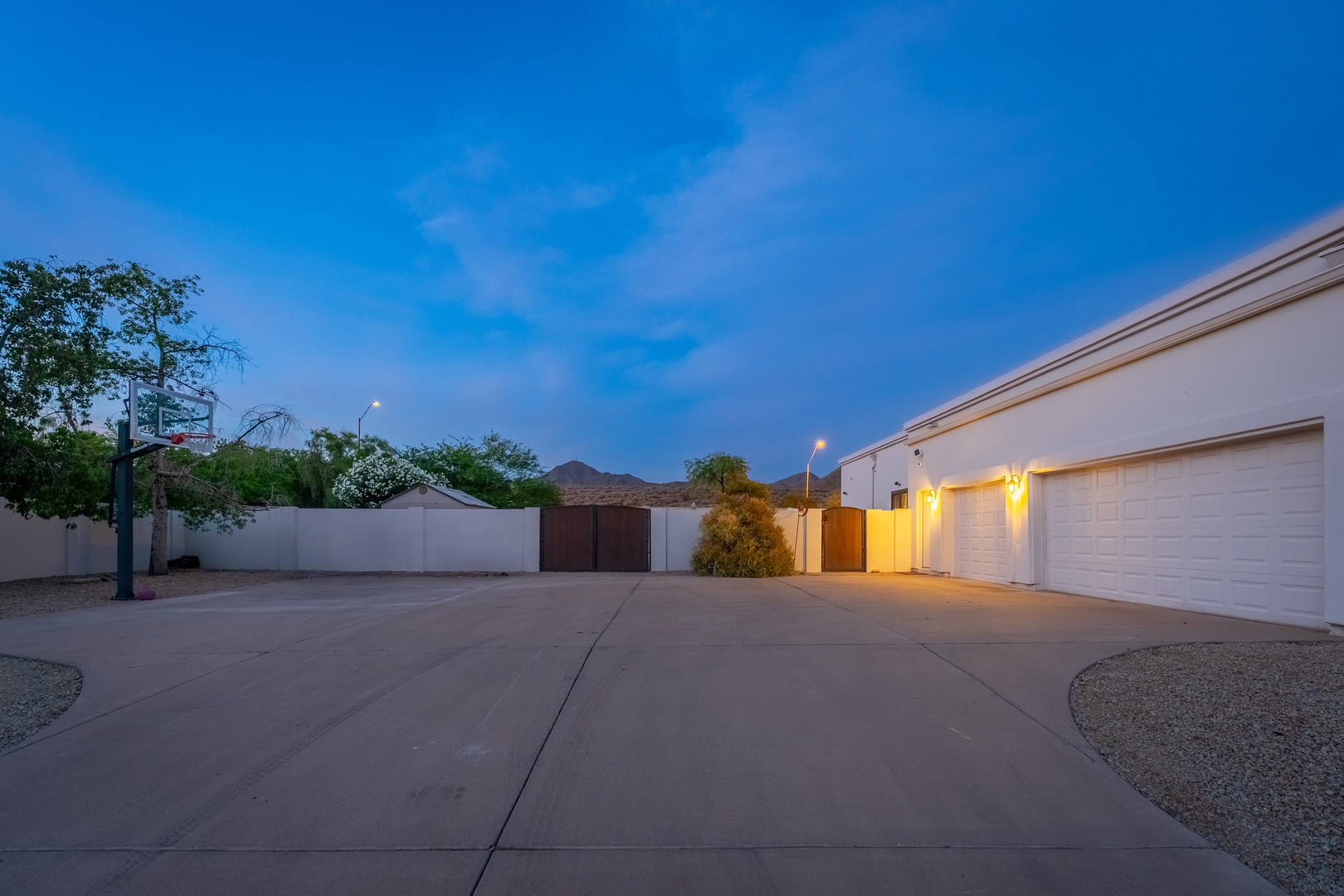 A spacious driveway leads to the property entrance and garage, framed by mountain views and illuminated by warm evening lighting against a beautiful twilight sky.