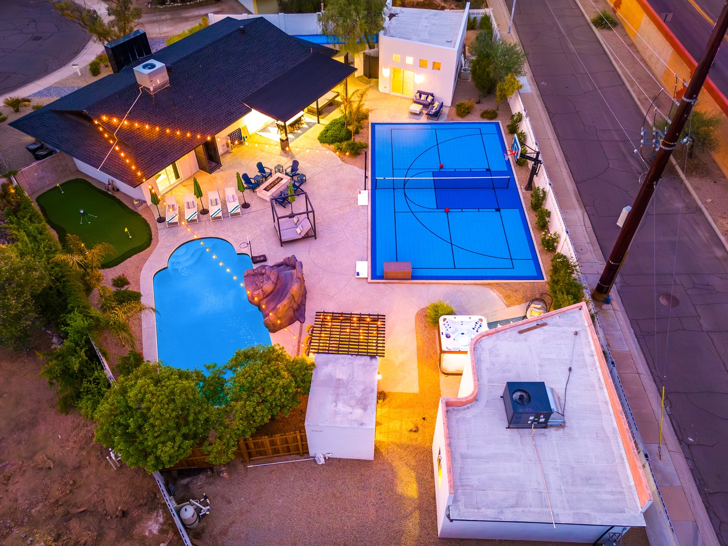 An aerial view captures the property's impressive outdoor recreation area, featuring a custom swimming pool, full-size sports court, hot tub, and putting green. The twilight scene showcases the property's extensive amenities and surrounding neighborhood.