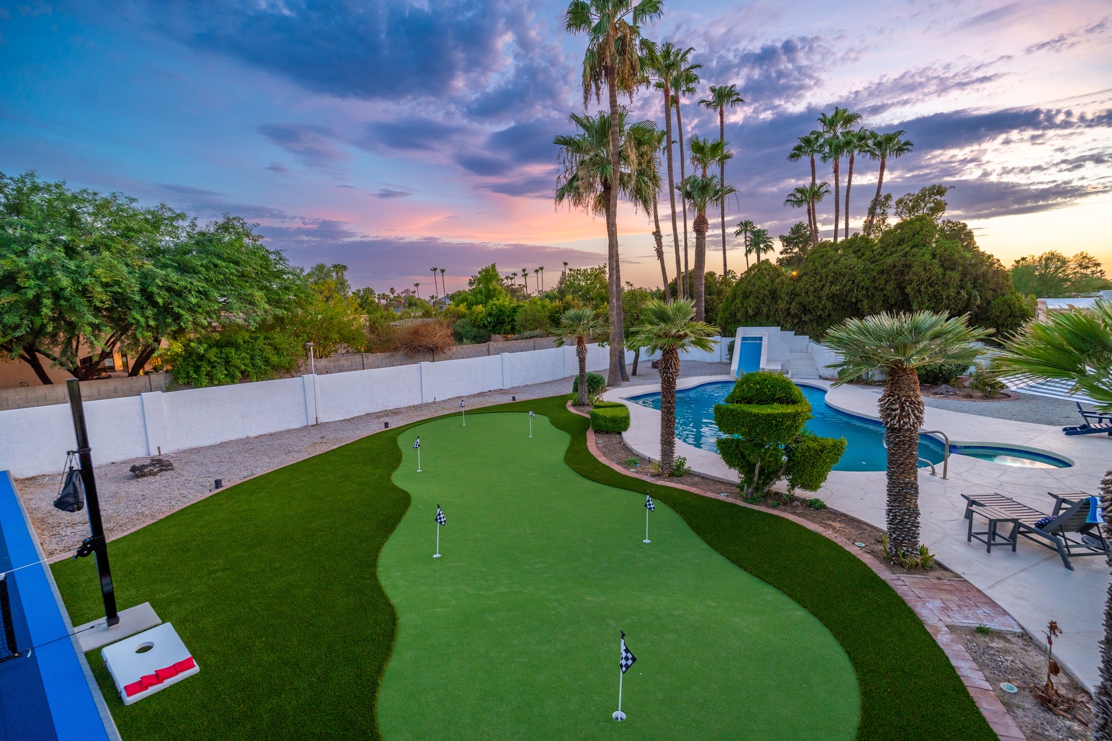 Private backyard oasis featuring a custom putting green, sparkling pool, and tropical landscaping surrounded by towering palms at sunset.