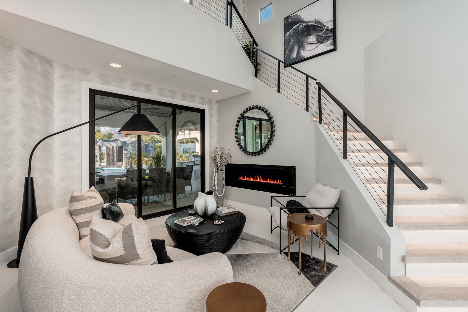 Sink into the plush curved sofa and feel the warmth of the modern fireplace as you unwind in this stunning two-story living space with sleek design and pool views.