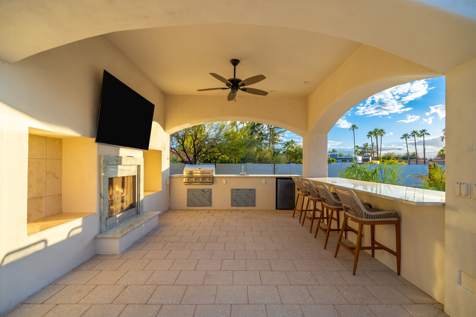 Step into your covered outdoor oasis, where a full bar, cozy fireplace, and entertainment center create the perfect spot for gathering with loved ones against stunning mountain and palm tree views.