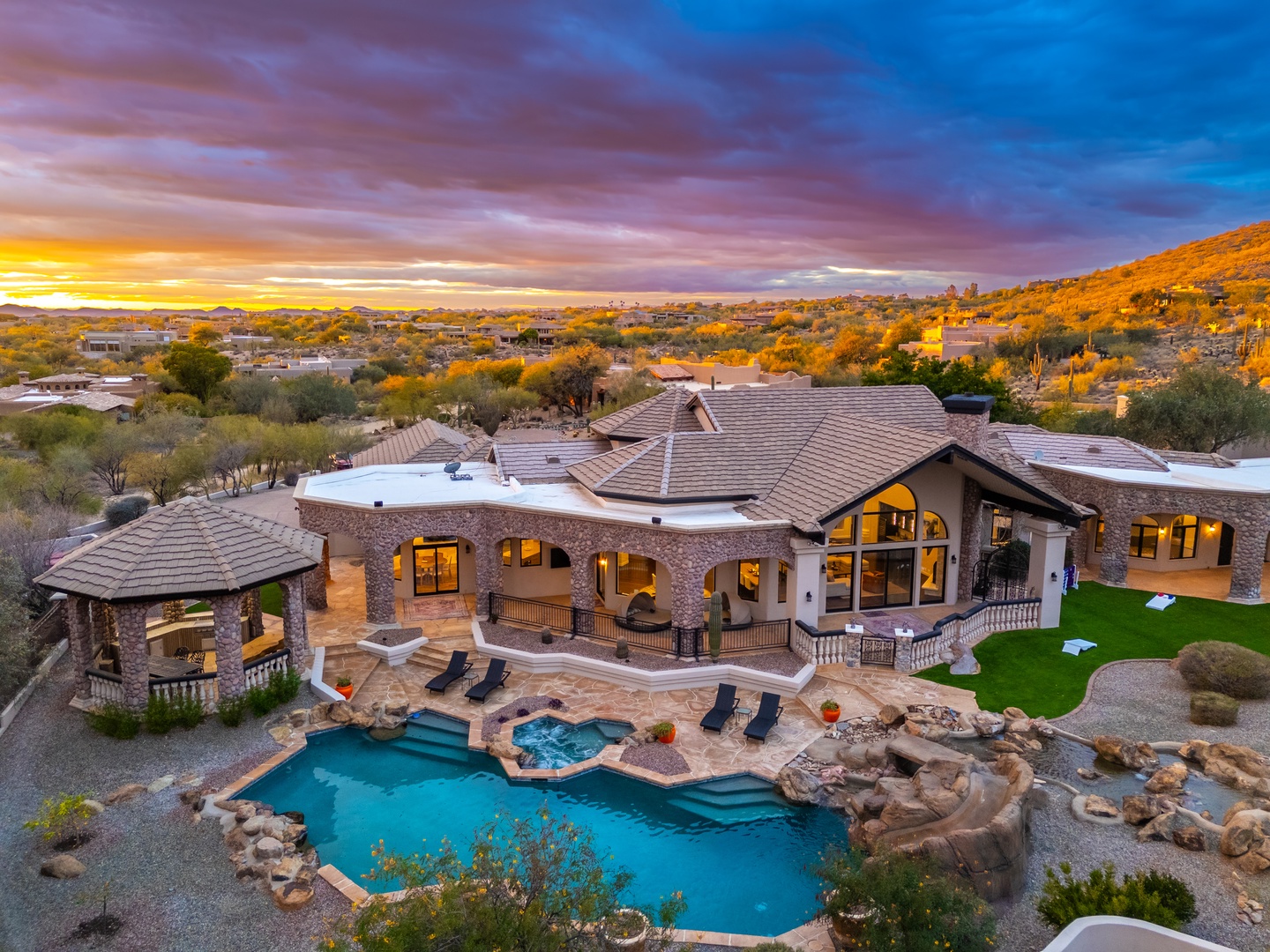 Stunning desert estate nestled in scenic hills, featuring a lagoon-style pool, spa, covered gazebo, and expansive outdoor spaces captured at golden hour.