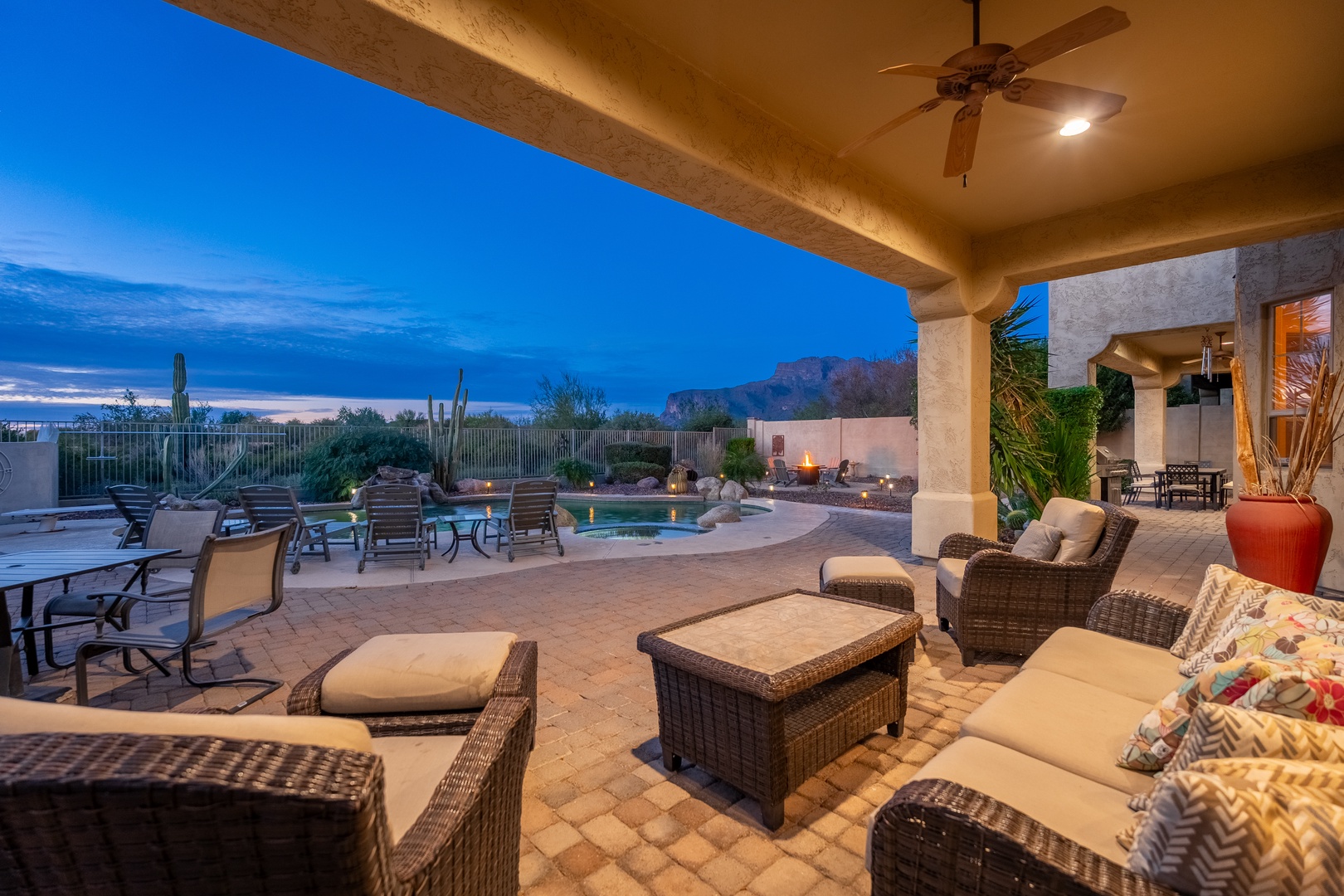 Relax in plush seating on your covered patio as desert twilight paints the sky, with mountain views, pool access, and ambient lighting creating your perfect evening retreat.