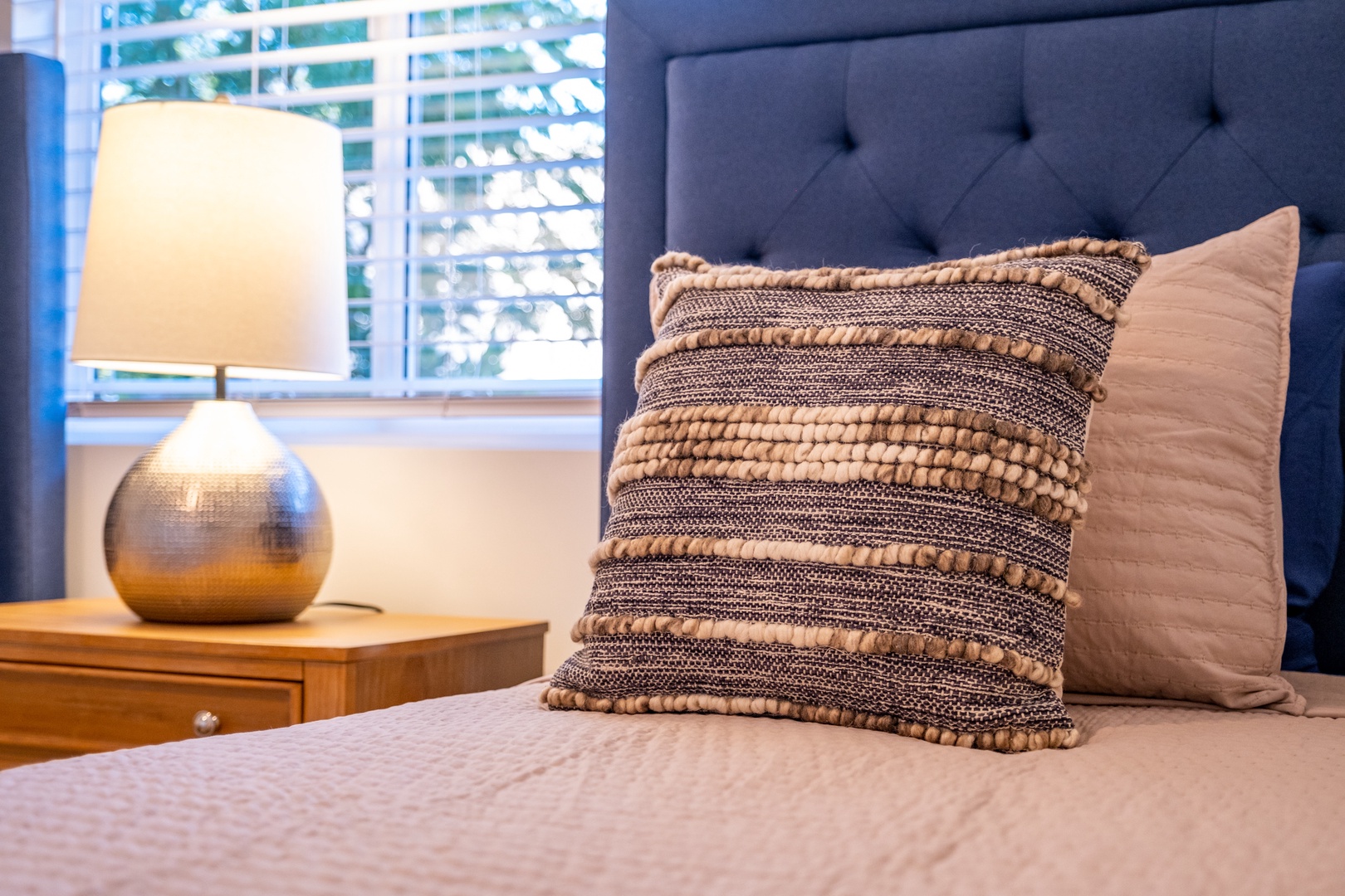 Unwind in your serene bedroom, where soft textured pillows rest against a plush headboard and natural light filters through, creating the perfect retreat after a day of exploring.