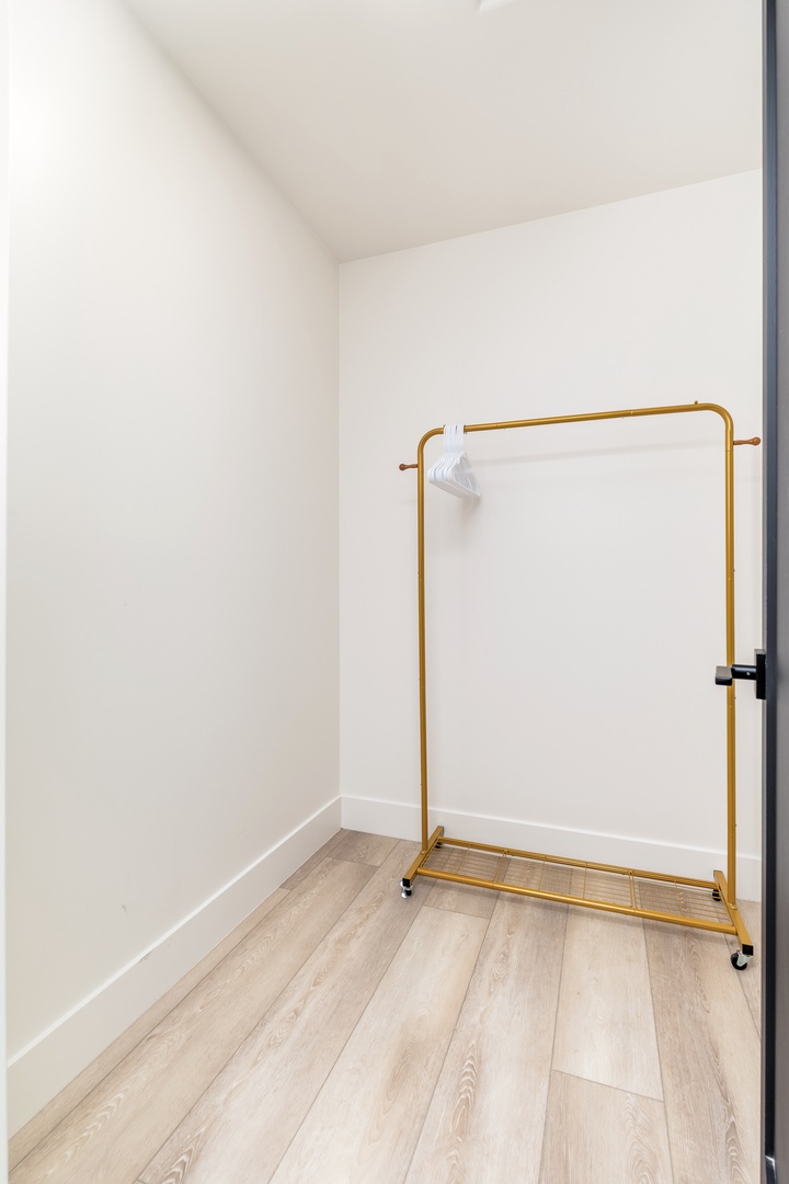 A spacious walk-in closet offers plenty of room for your wardrobe, with a stylish gold garment rack and hangers ready for unpacking.