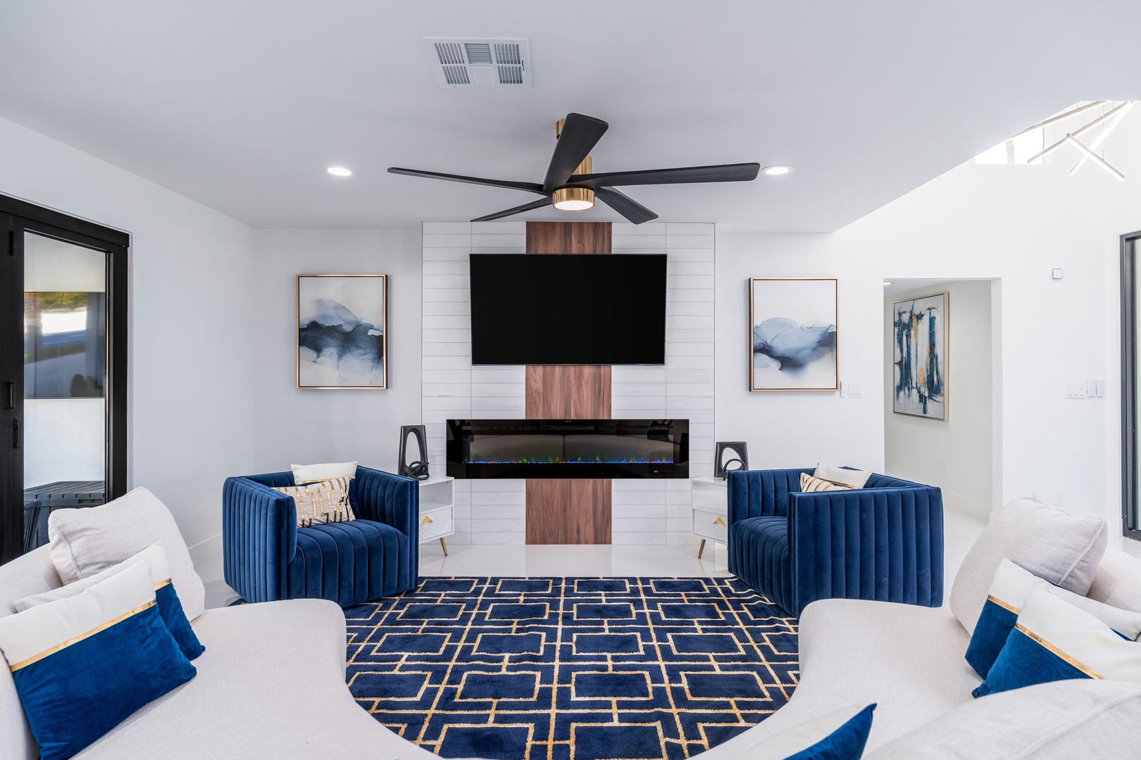 Your elegant living room features plush navy velvet chairs, a modern fireplace, and stylish artwork—ideal for cozy evenings or entertaining guests in refined comfort.