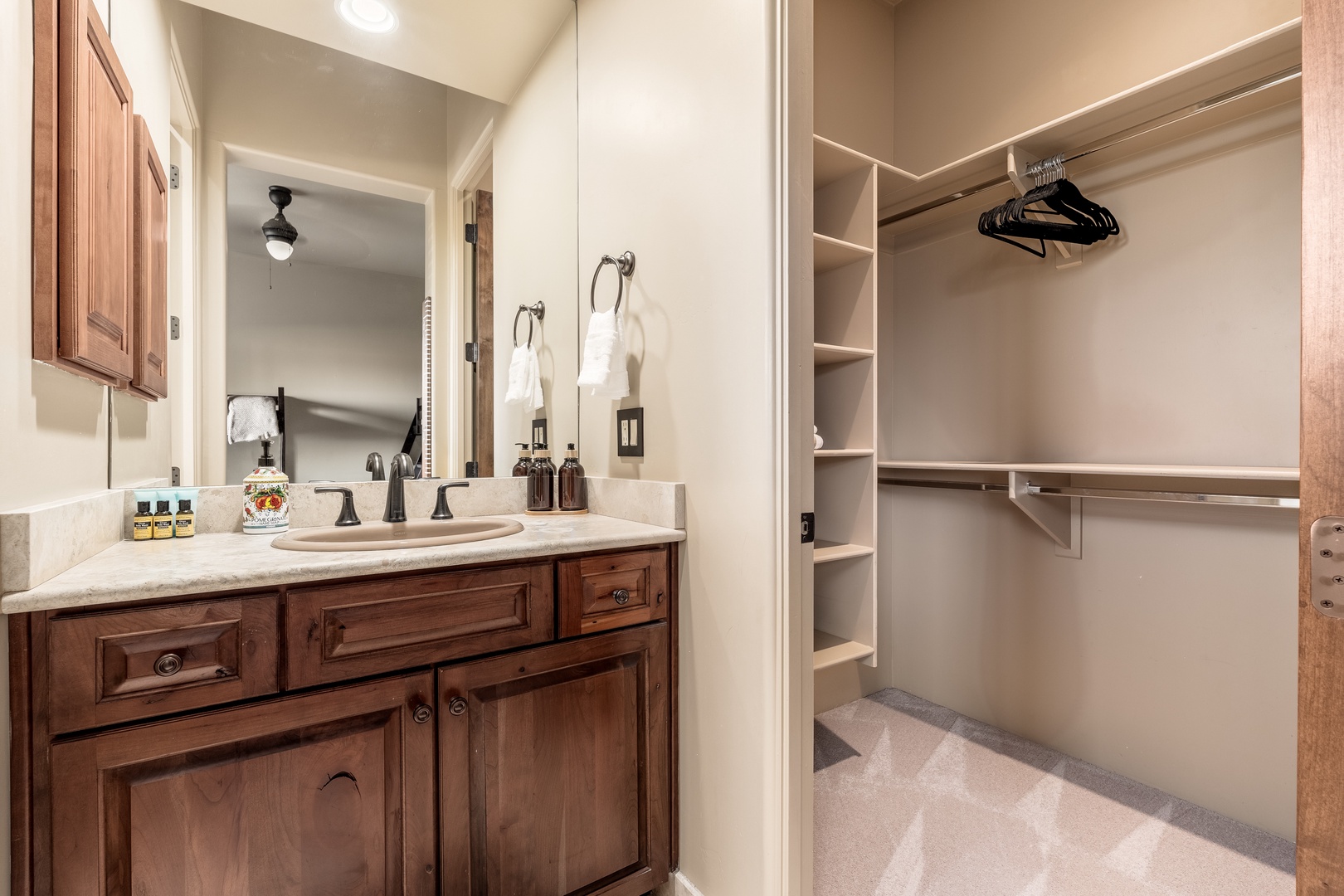 Your private bathroom features warm wood cabinetry, a spacious vanity, and a walk-in closet with organized shelving and hanging space for all your belongings.